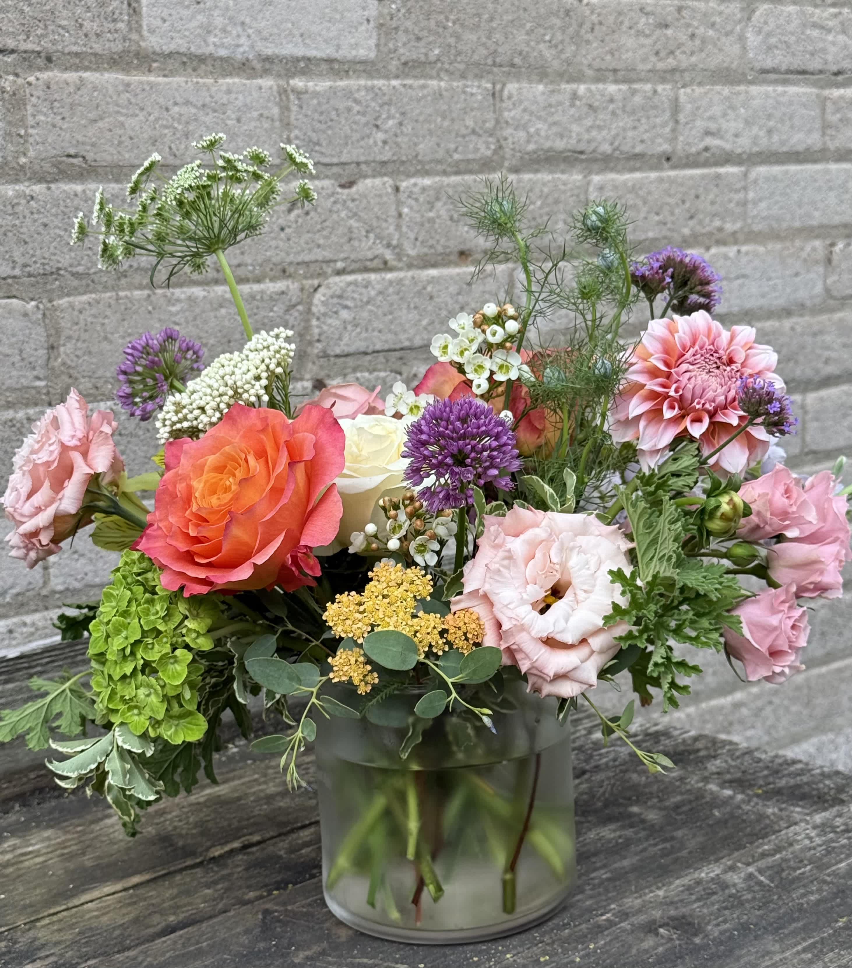 Mixed bouquet of pink, orange, purple, and white flowers in a glass vase