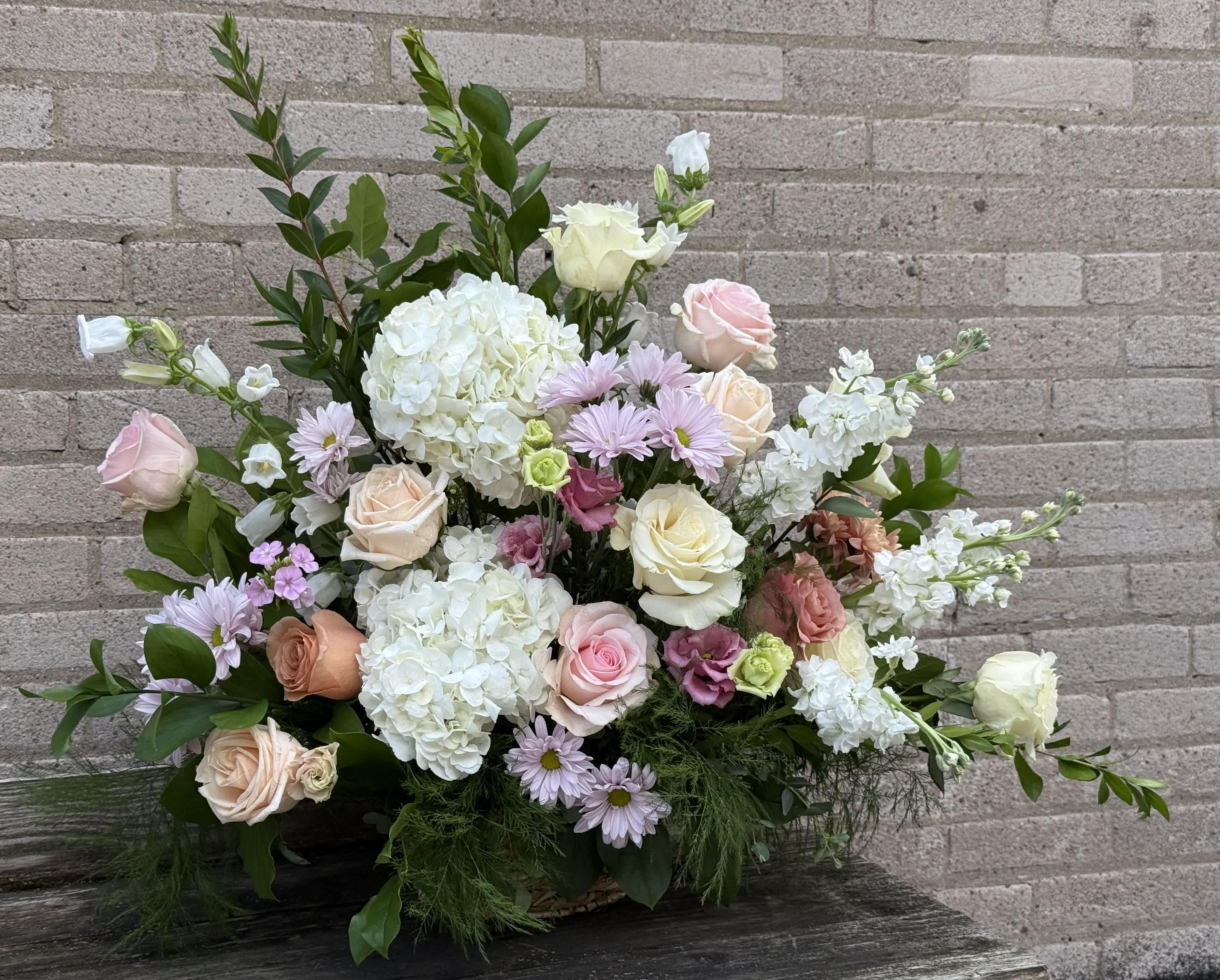 Pastel bouquet with roses, hydrangeas, and daisies against a brick wall