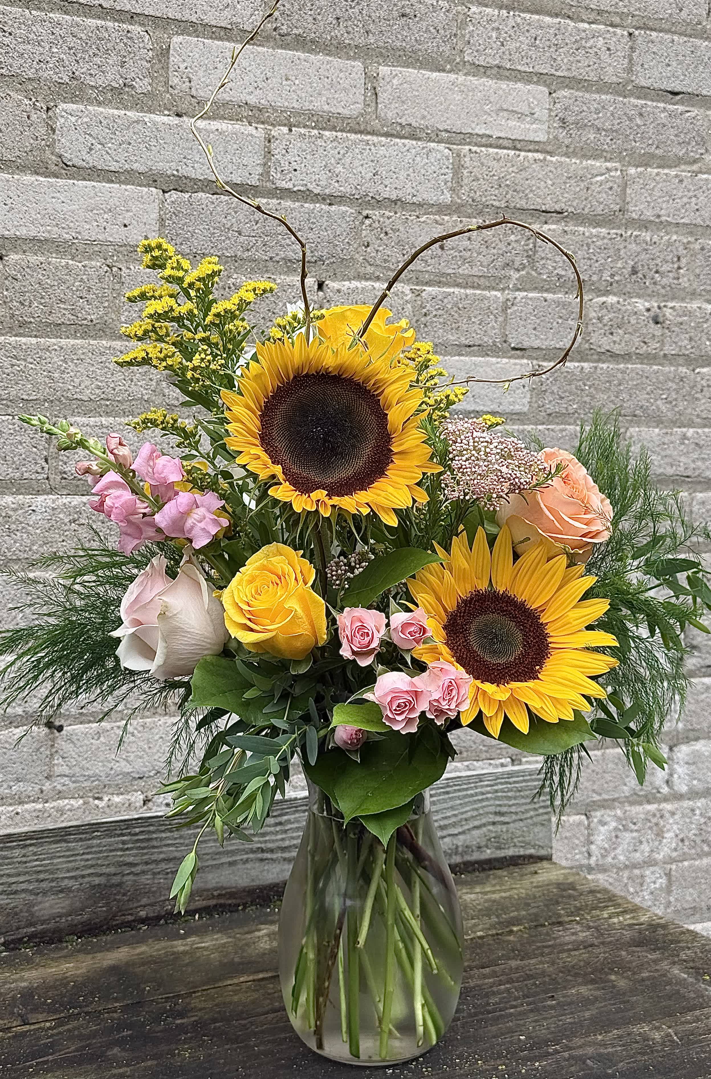 Sunflower and rose bouquet in a glass vase with curly branches