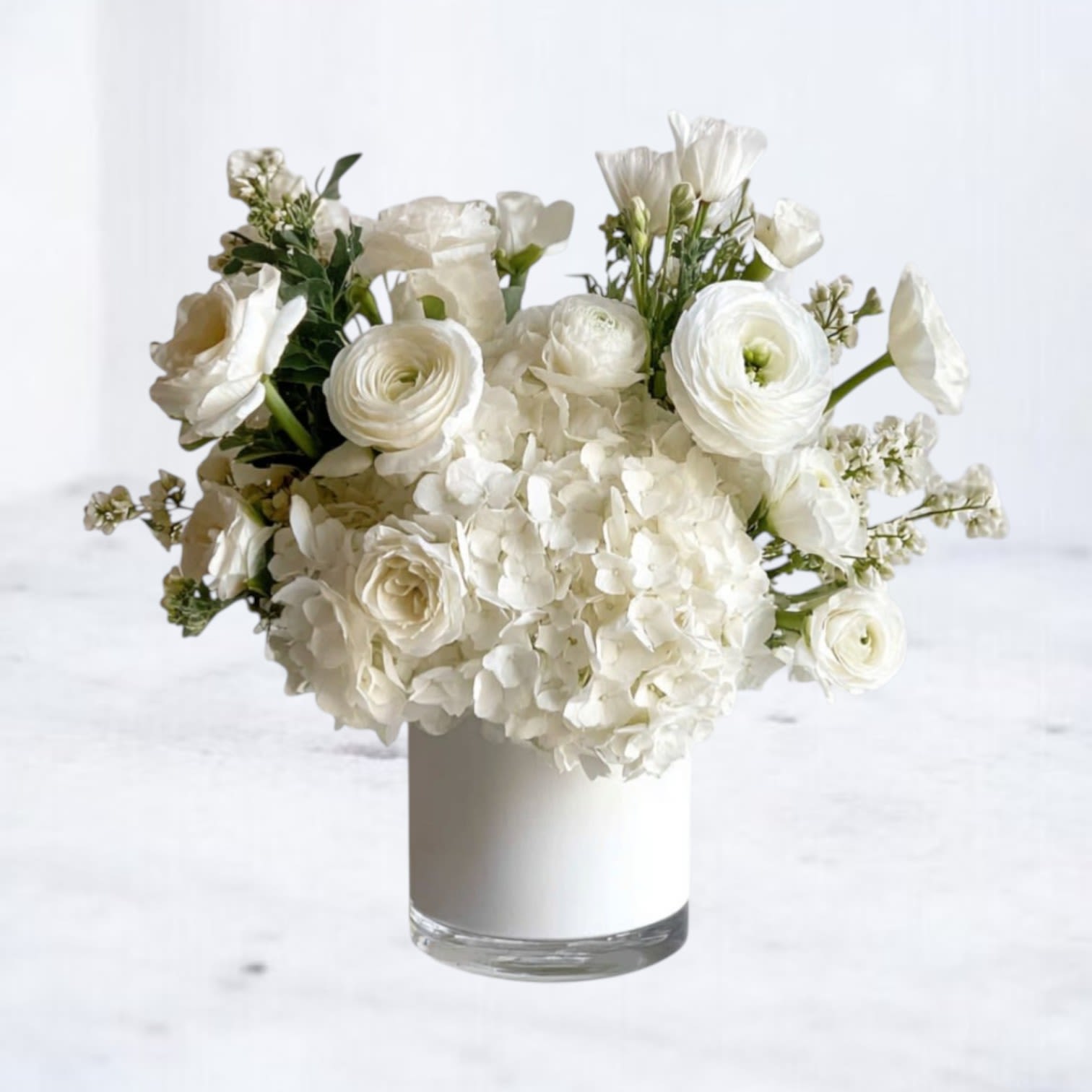 Pure Grace Bouquet - The Pure Grace Bouquet is a stunning all-white arrangement designed to embody elegance and serenity. Featuring fluffy hydrangea, delicate ranunculus, creamy roses, and seasonal white blooms, this bouquet is arranged in a sleek glass vase for a refined finish. Its timeless palette makes it a versatile choice for sympathy tributes, weddings, anniversaries, or as a sophisticated everyday gift.  Available for same-day flower delivery in Galveston, Houston, and surrounding areas, this bouquet is the perfect way to honor life’s most meaningful moments with beauty and grace.  Substitution Disclaimer: Due to seasonal availability, some blooms may be replaced with similar varieties of equal or greater value to maintain the design’s look and integrity. Your arrangement will always reflect the same spirit, palette, and premium quality.