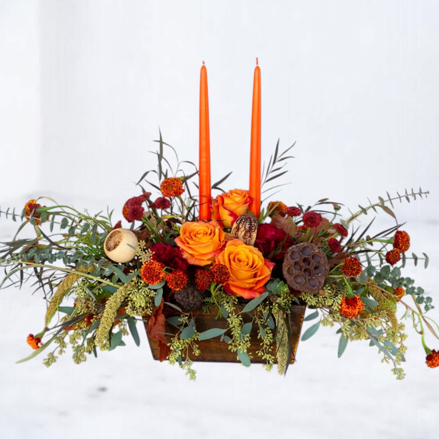 Orange roses in a low wooden container with two tall orange candles