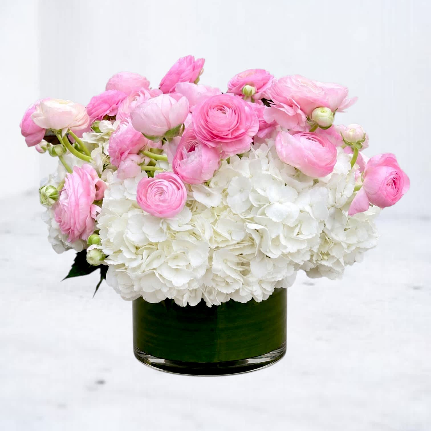 Pink ranunculus and white hydrangeas in a green glass vase