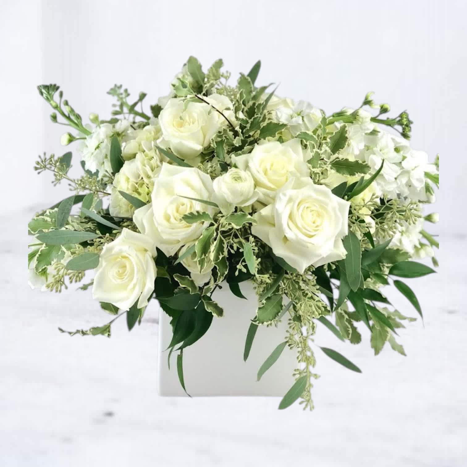 White rose arrangement in a white square vase