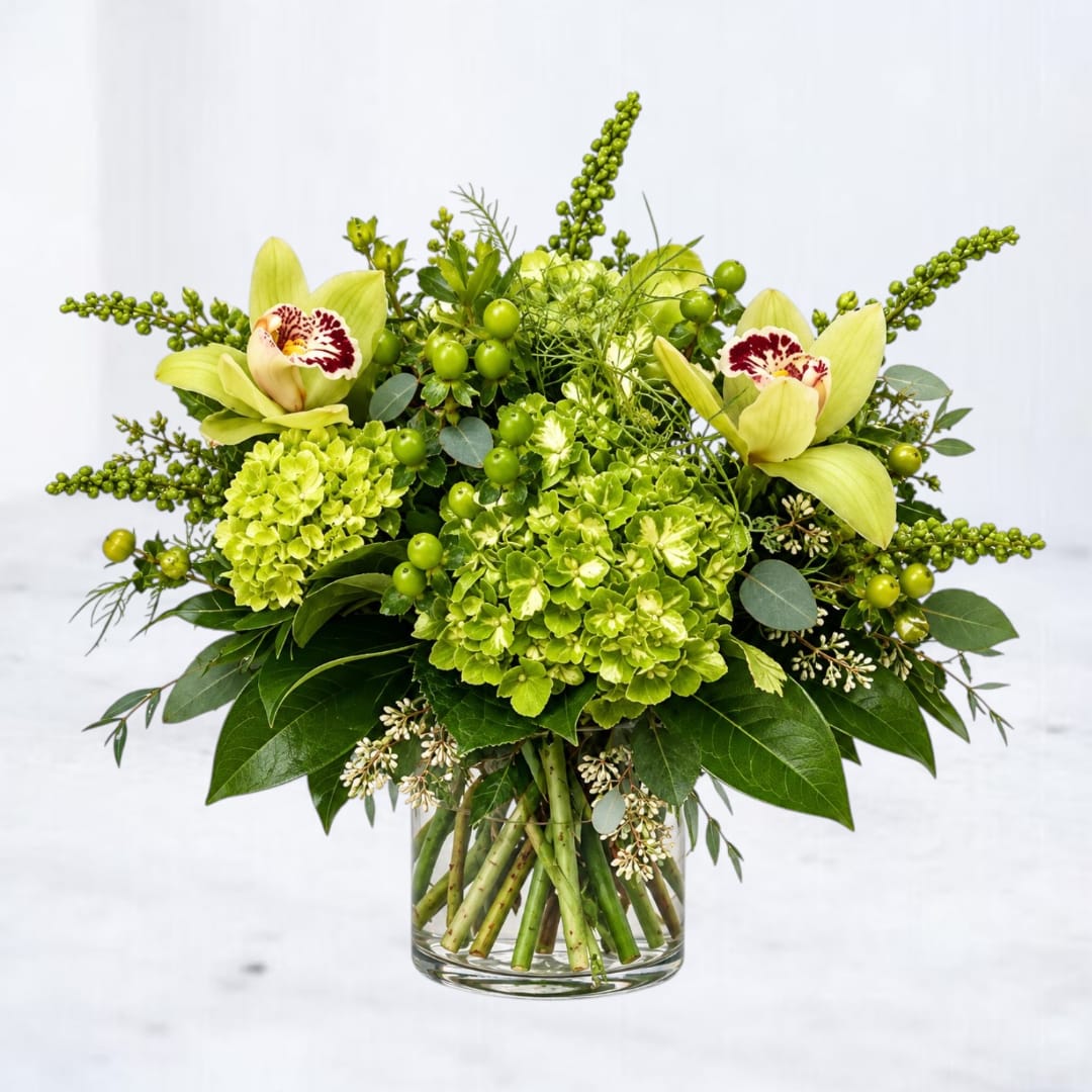 Green floral arrangement with orchids and hydrangeas in a glass vase