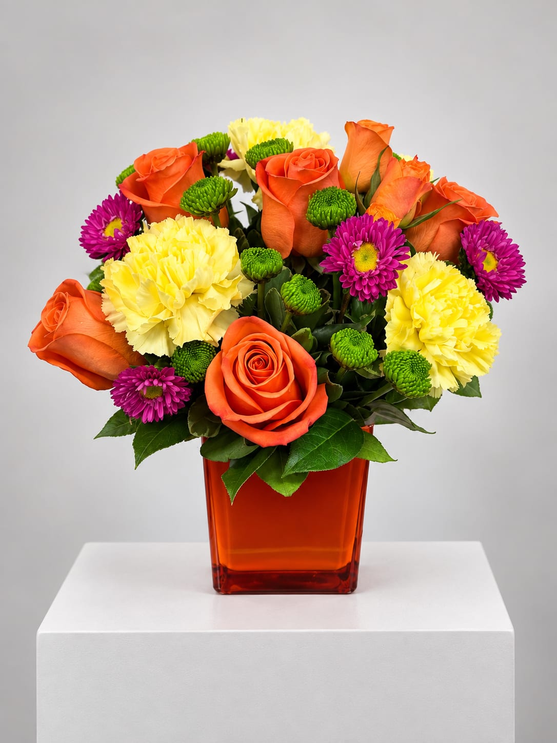 Orange roses, yellow carnations, and purple daisies in an orange vase