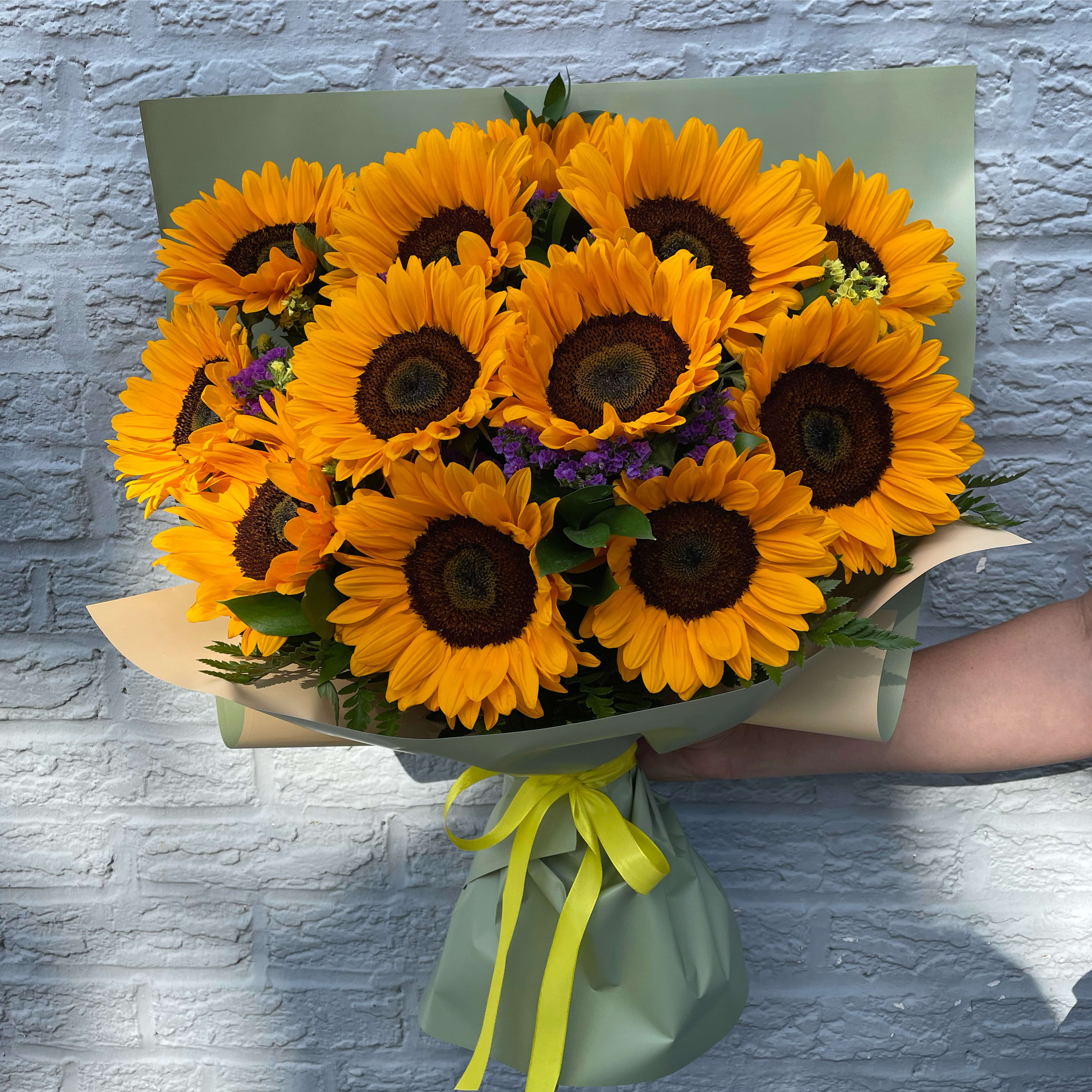 Bouquet of bright yellow sunflowers wrapped in green paper with a yellow ribbon