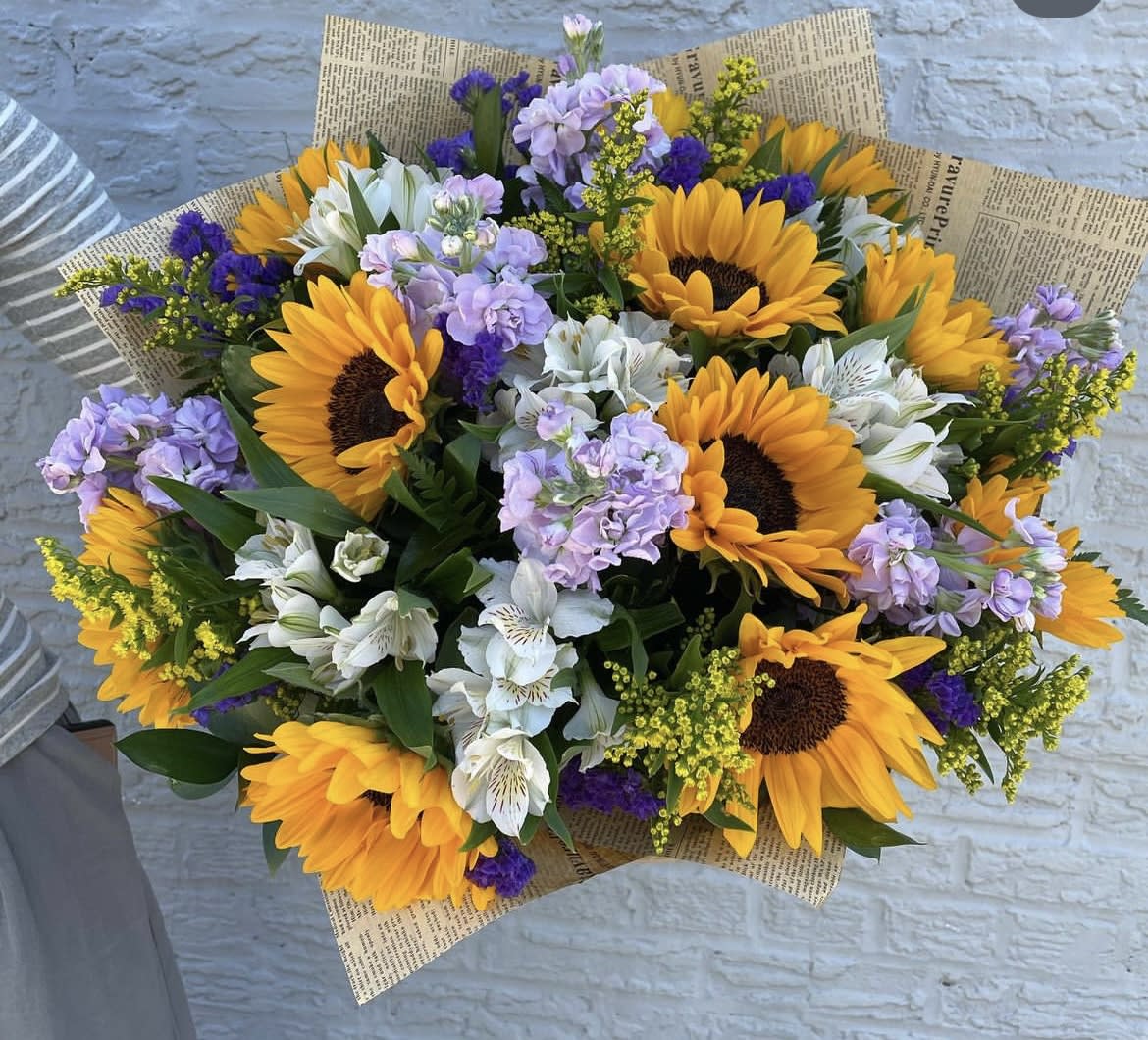 Bouquet of sunflowers, white alstroemeria, and lavender flowers in newspaper wrap