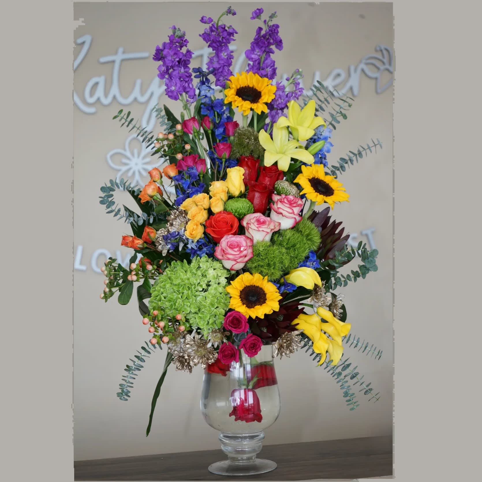 Tall mixed arrangement with sunflowers, roses, lilies, hydrangea and calla lilies in a clear glass vase