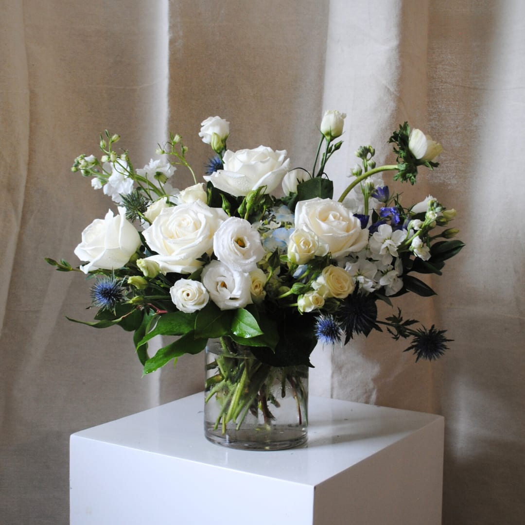 White rose bouquet in a clear glass vase with blue accents