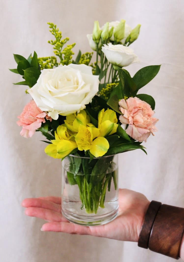 Mini Buttercream - A bright, cheerful hand-held arrangement with white roses, soft peach carnations, yellow alstroemeria, and solidago. Styled in a small glass vase with clean greenery for a fresh, modern look.