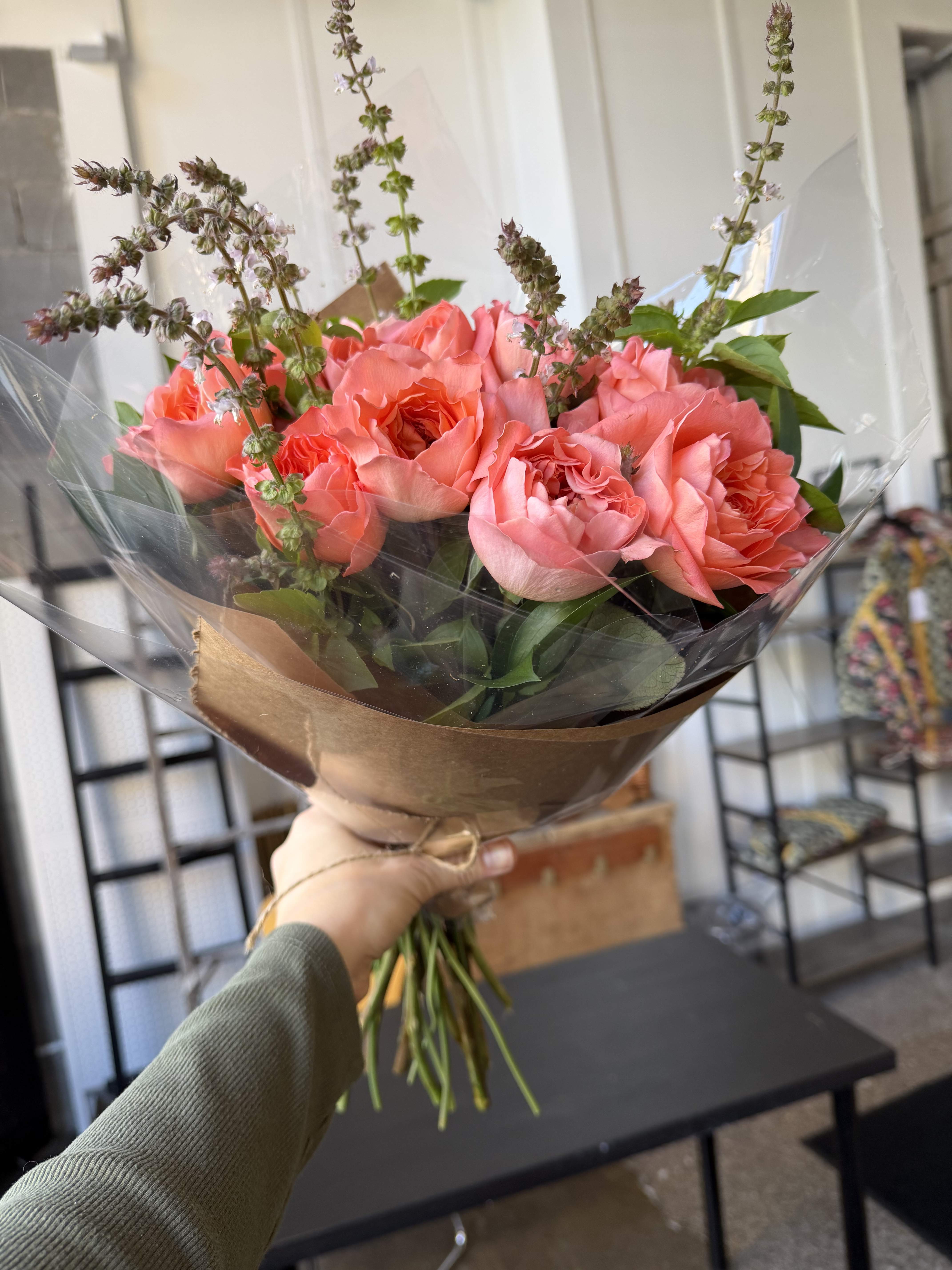 Handheld bouquet of pink roses wrapped in brown paper and clear plastic