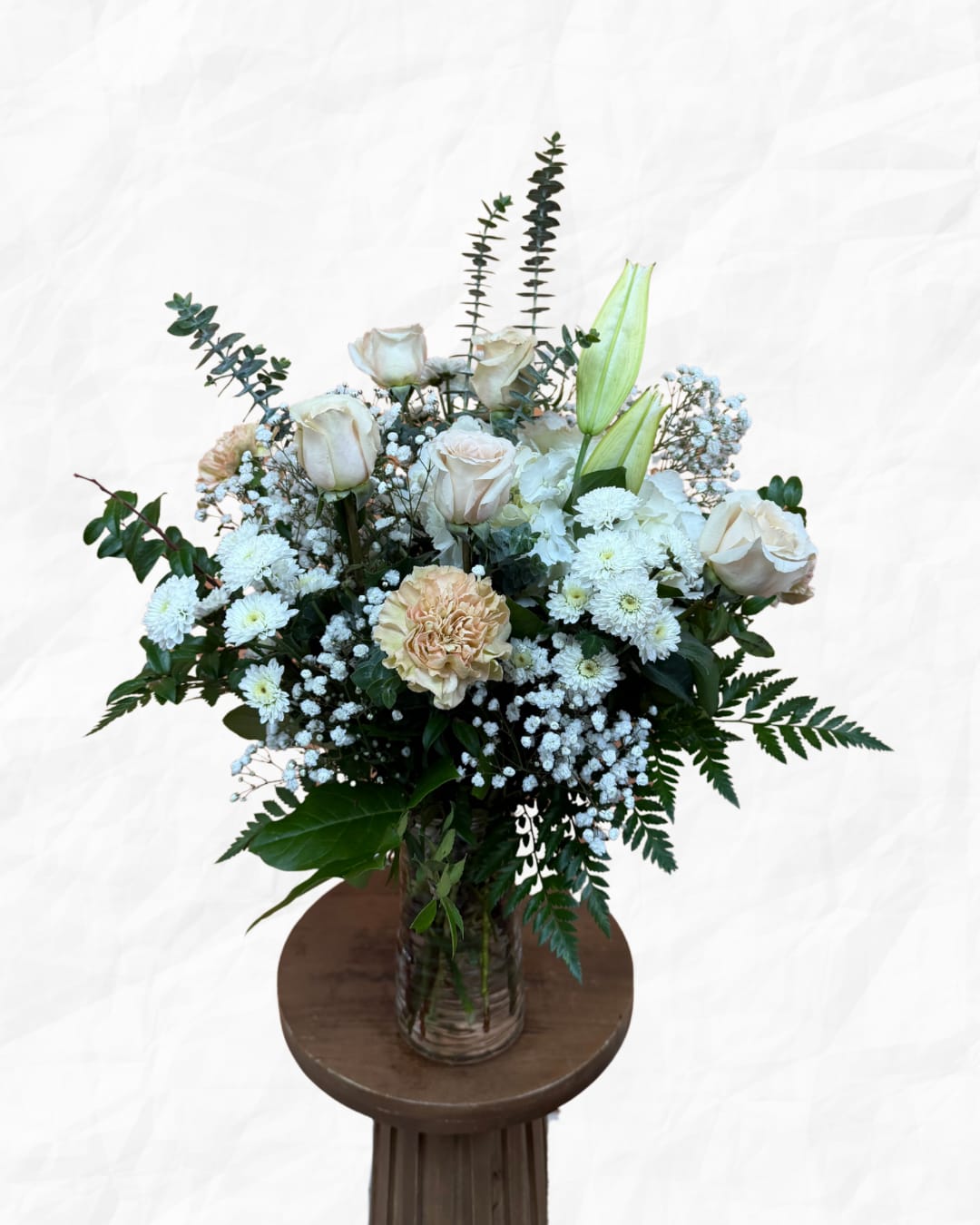 White roses and lilies arranged in a glass vase with greenery