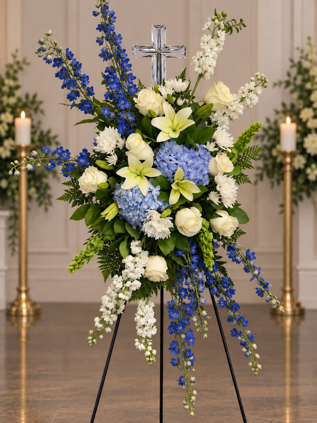 Tall funeral spray with blue and white flowers and a silver cross