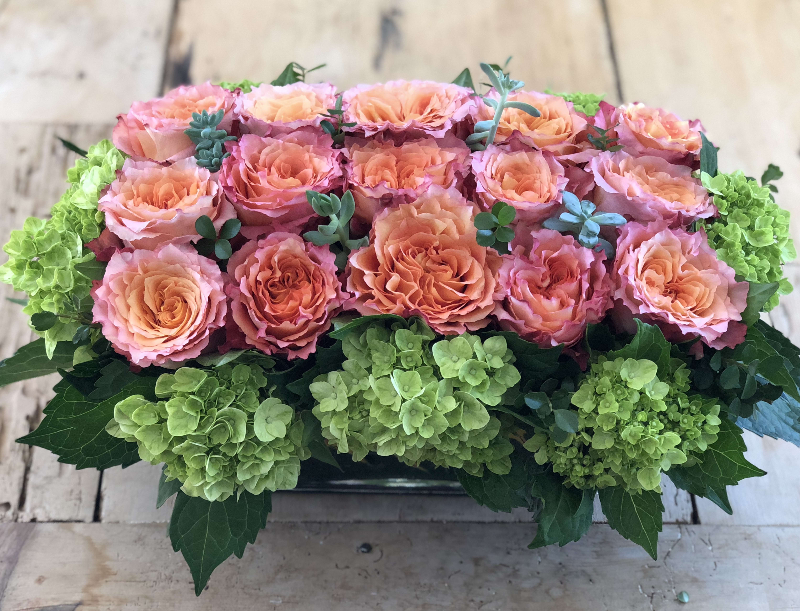 Peach and pink roses arranged with green hydrangeas in a low rectangular container