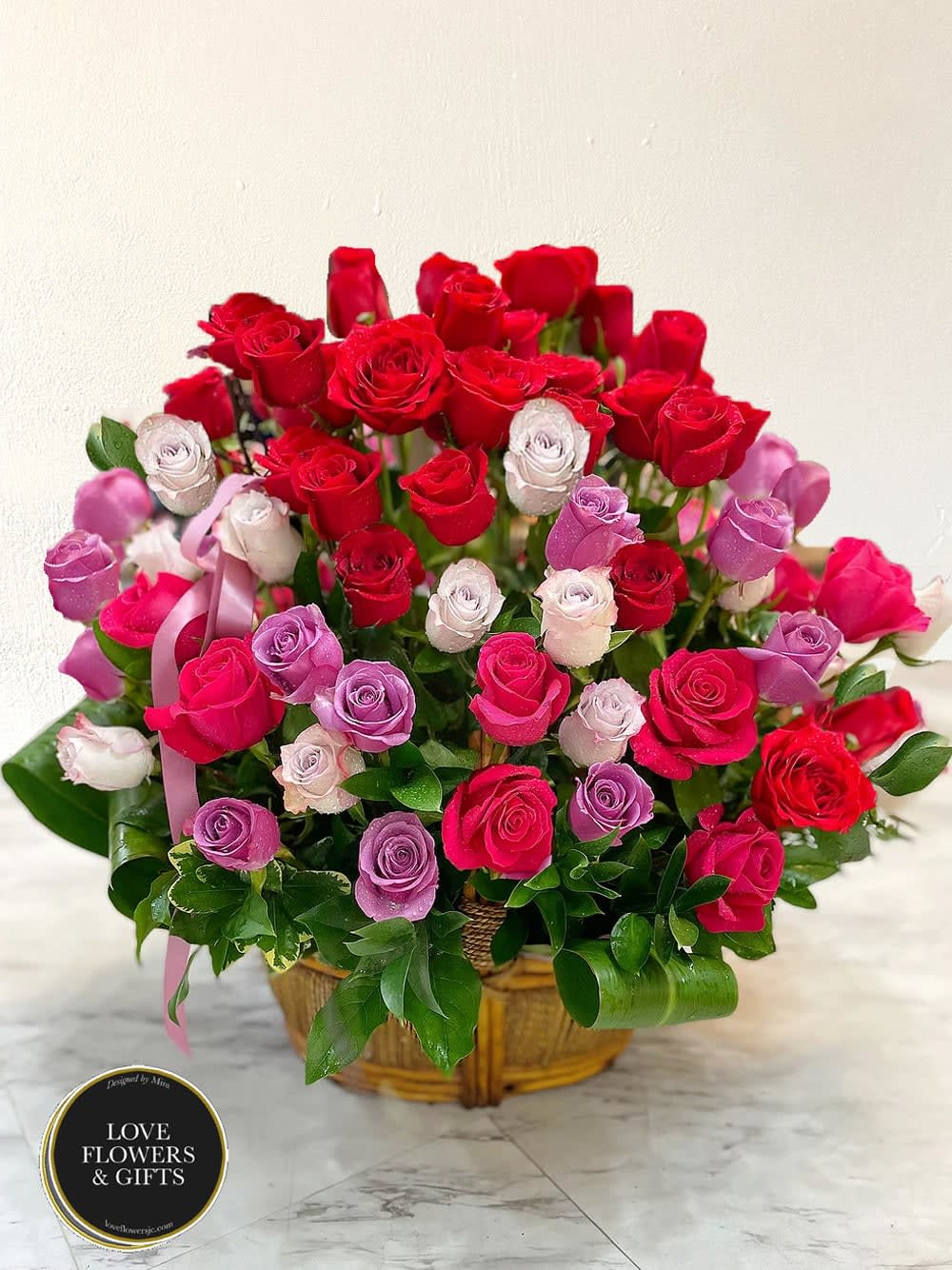 Basket arrangement of red, pink, and lavender roses displayed on a marble surface