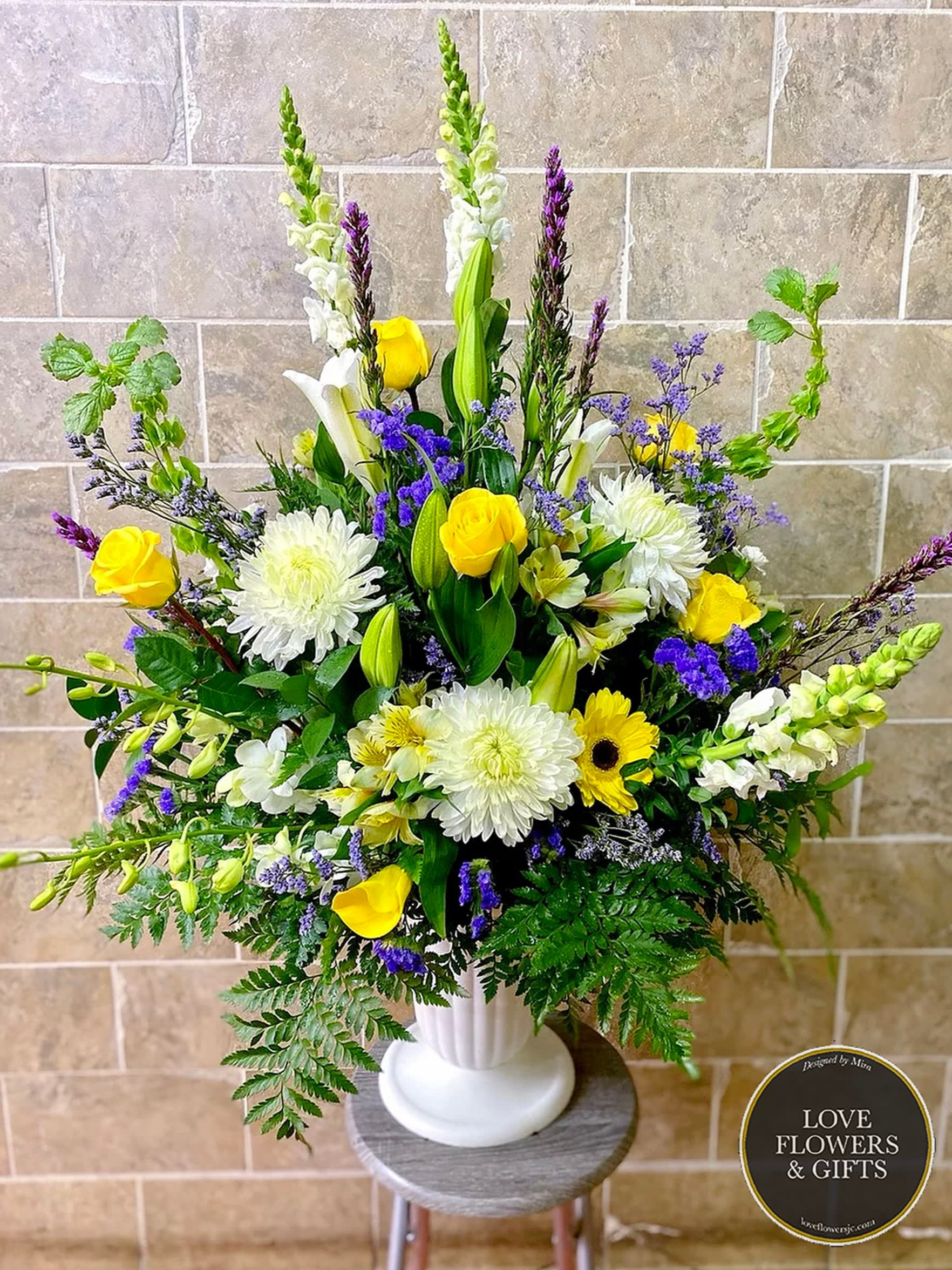 Tall yellow, white, and purple flower arrangement in a white pedestal vase