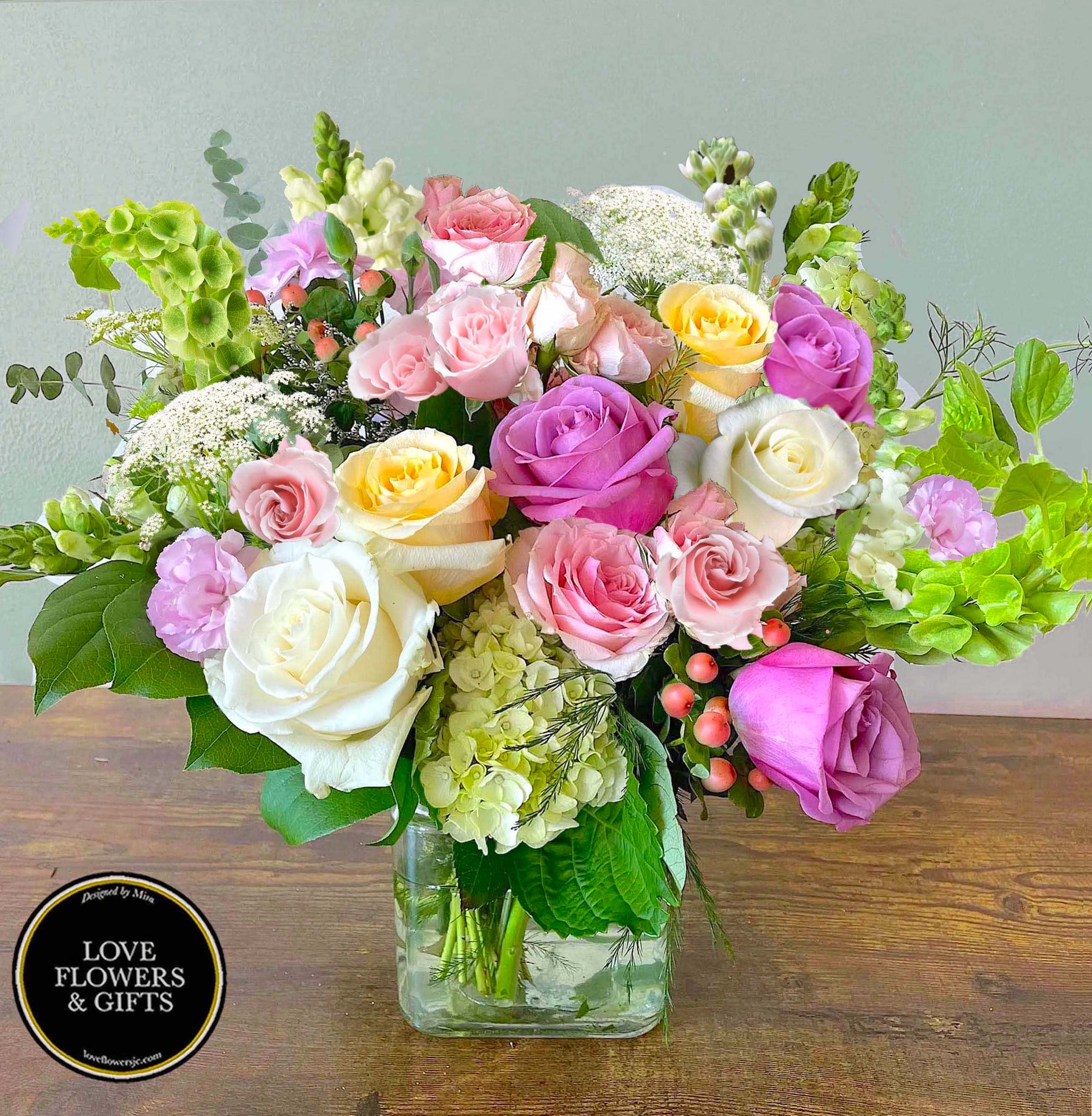Pastel roses, hydrangea, and mixed blooms arranged in a clear square glass vase