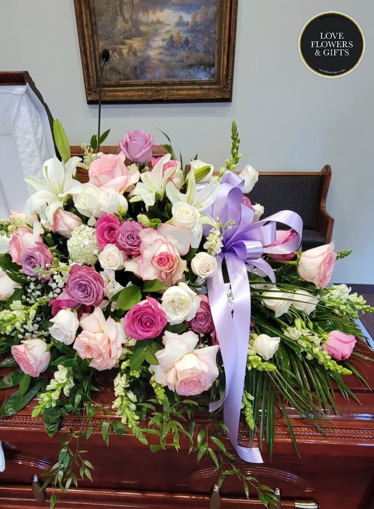 Pink, lavender, and white rose and lily casket spray with a lavender ribbon.
