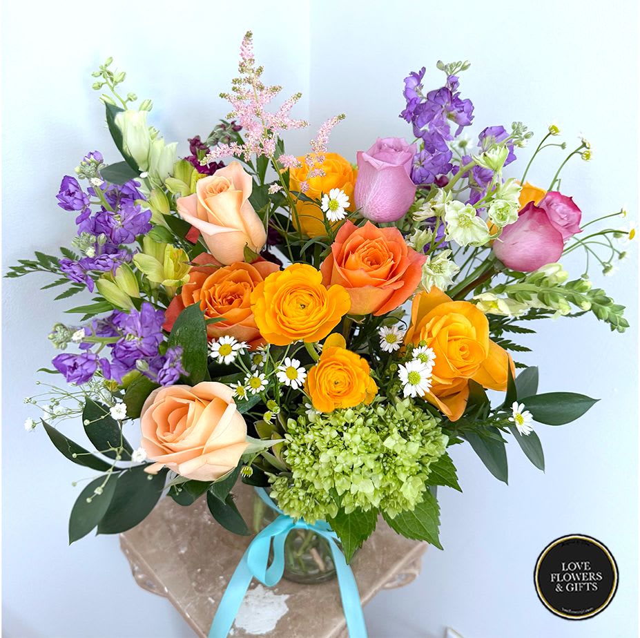 Bright mixed bouquet of orange and peach roses, yellow blooms, purple flowers and white daisies in a glass vase