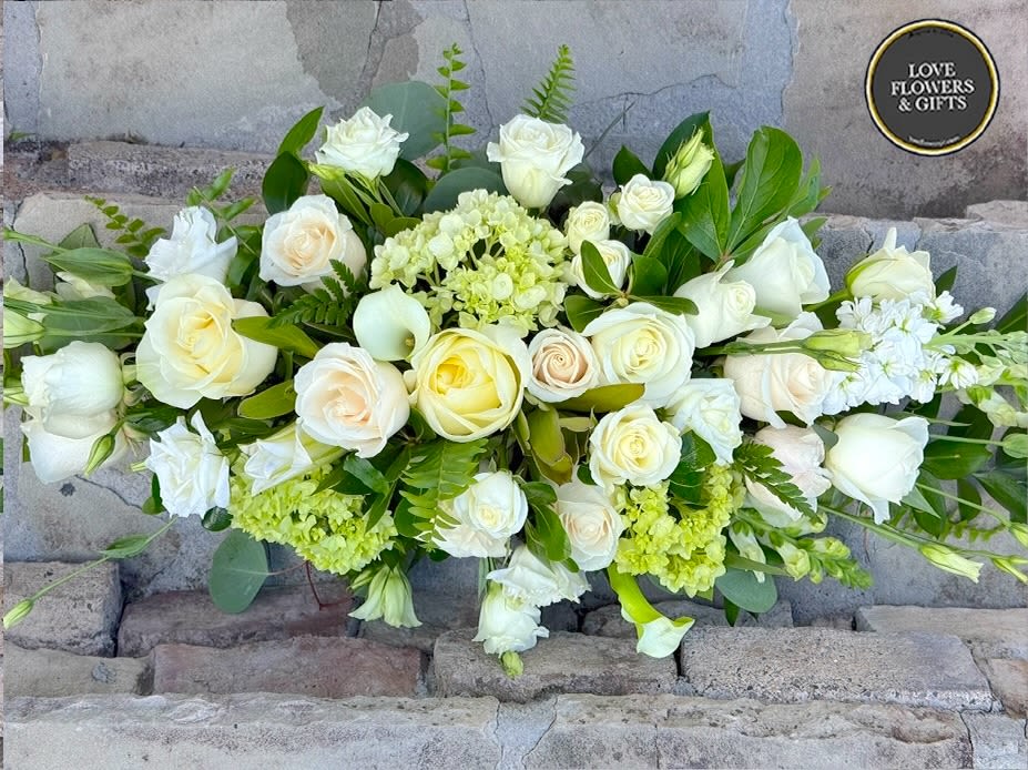 Low arrangement of white and cream roses with soft green blooms in an elongated design