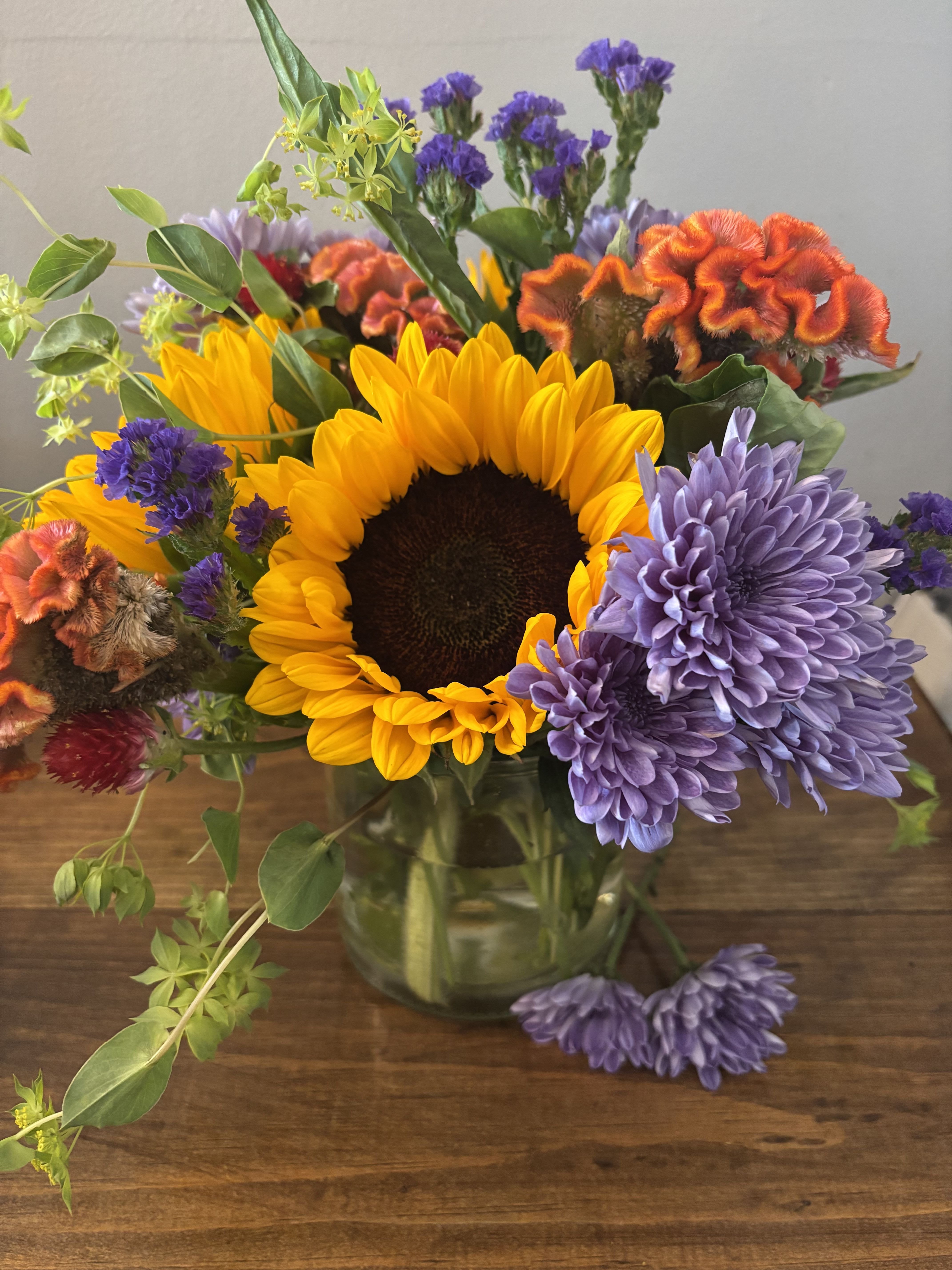 Mixed bouquet with a sunflower, purple chrysanthemums, and orange cockscomb in a glass vase