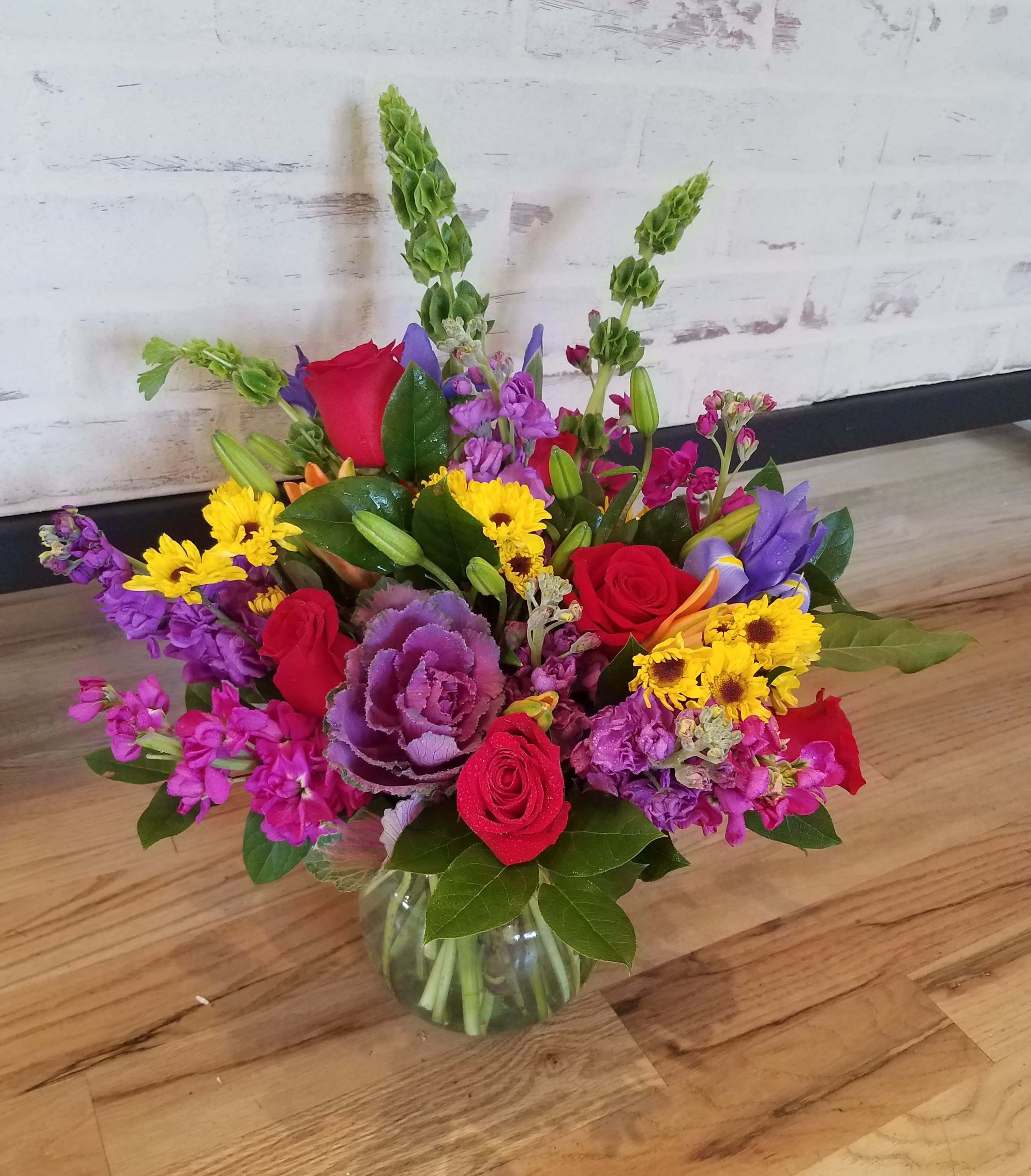 Mixed bouquet of red roses, purple flowers, and yellow daisies in a glass vase