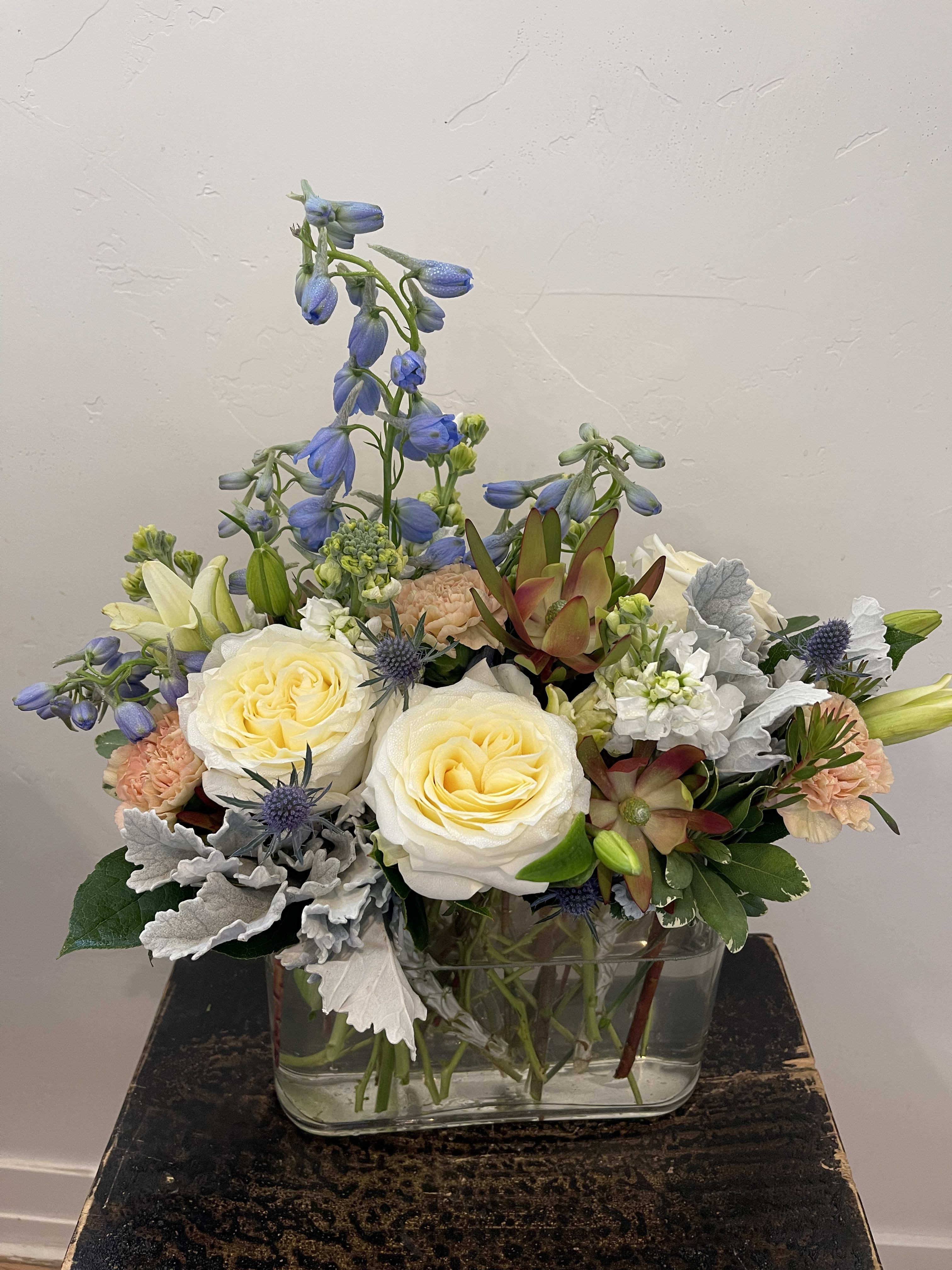 Mixed bouquet in a clear glass vase with cream roses and blue flowers