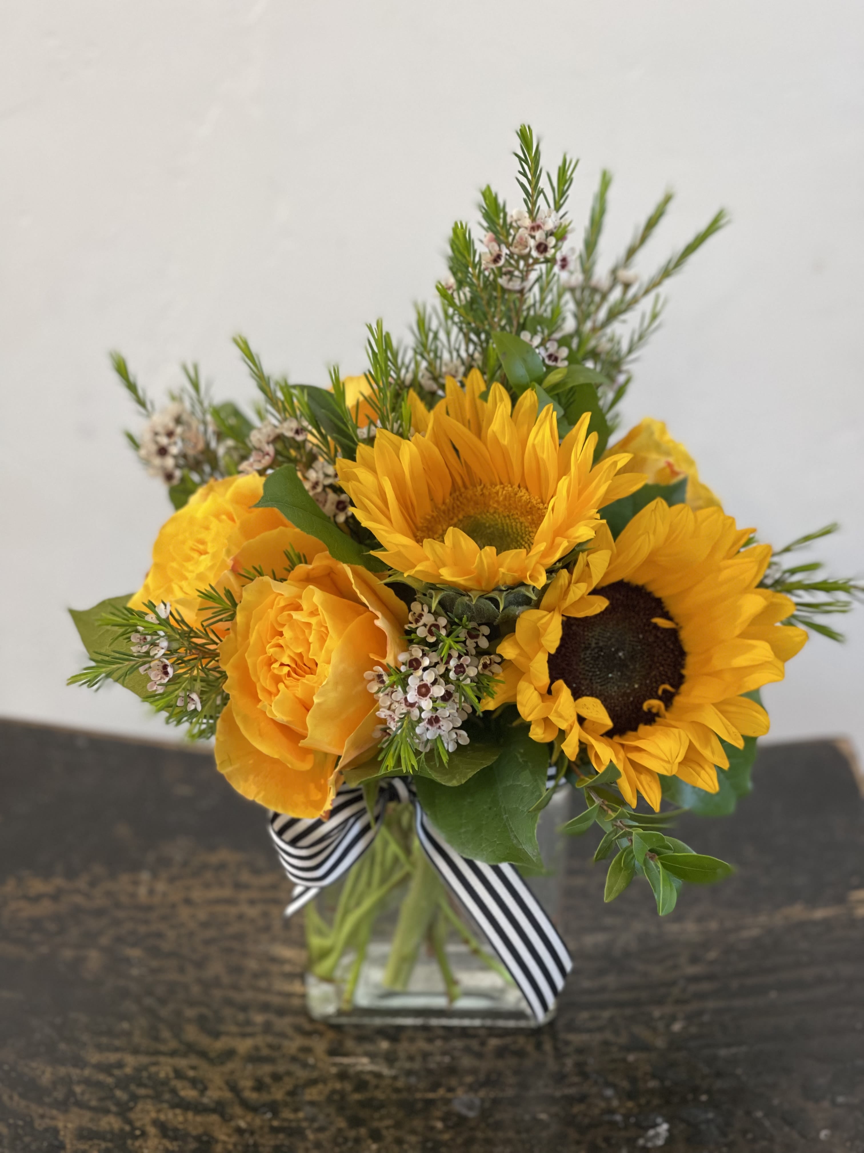 Yellow sunflower and rose bouquet in a glass vase with a striped ribbon