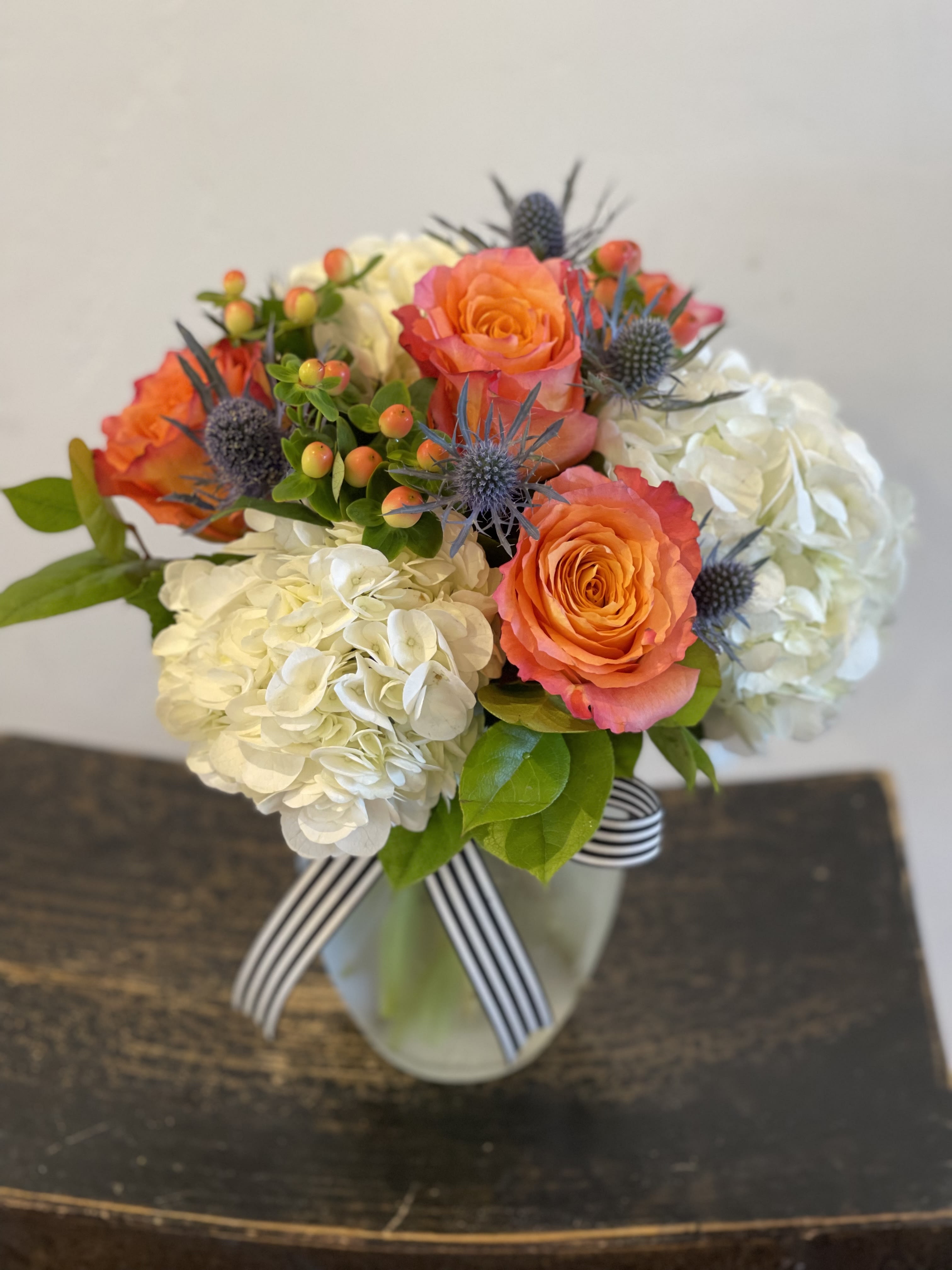 Cloud 9 - A lush arrangement of white cloud hydrangea, coral roses and hypericum with a touch of blue hypericum. Stands approximately 12" tall. 