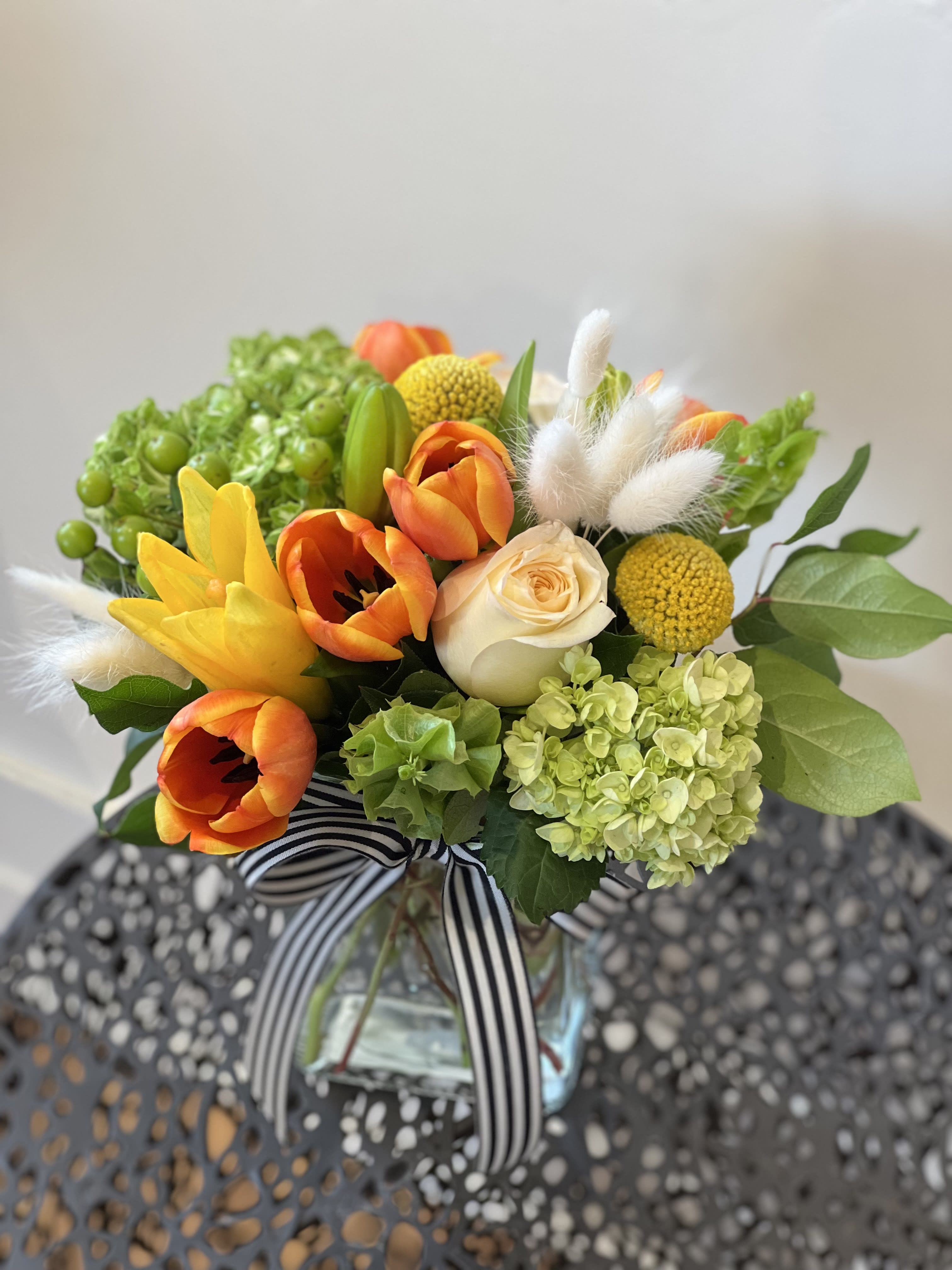 Gentle Blooms - A lovely soft and gentle arrangement designed in a rectangular glass vase. Filled with green hydrangeas, orange tulips, yellow asiatic lilies, bells of Ireland, craspedia, hypericum berries, candlelight roses and bleached bunny tail. 