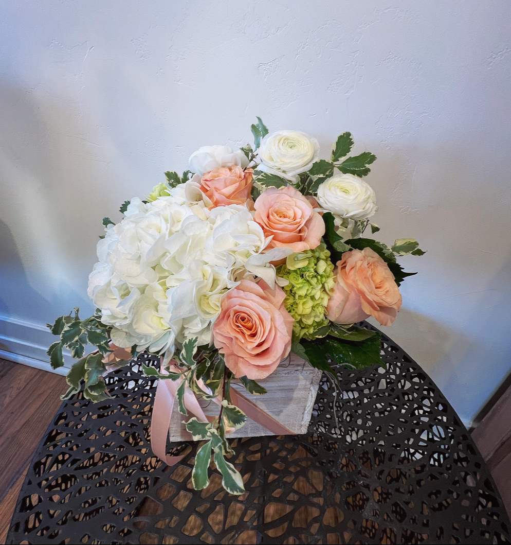 Low arrangement of white hydrangeas, peach roses, and white blooms in a rustic wooden box.