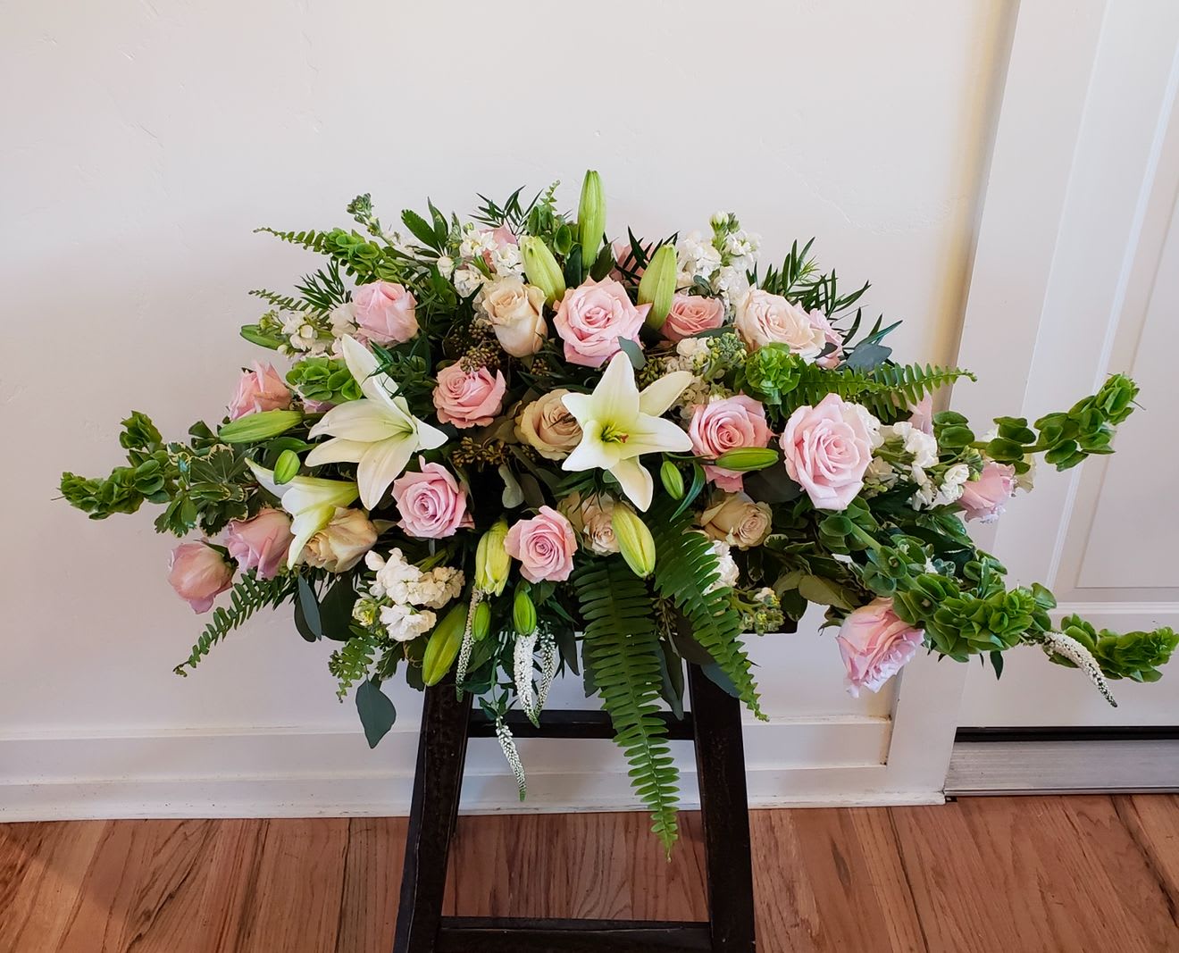 Pink roses and white lilies arranged in a low, wide display on a stand