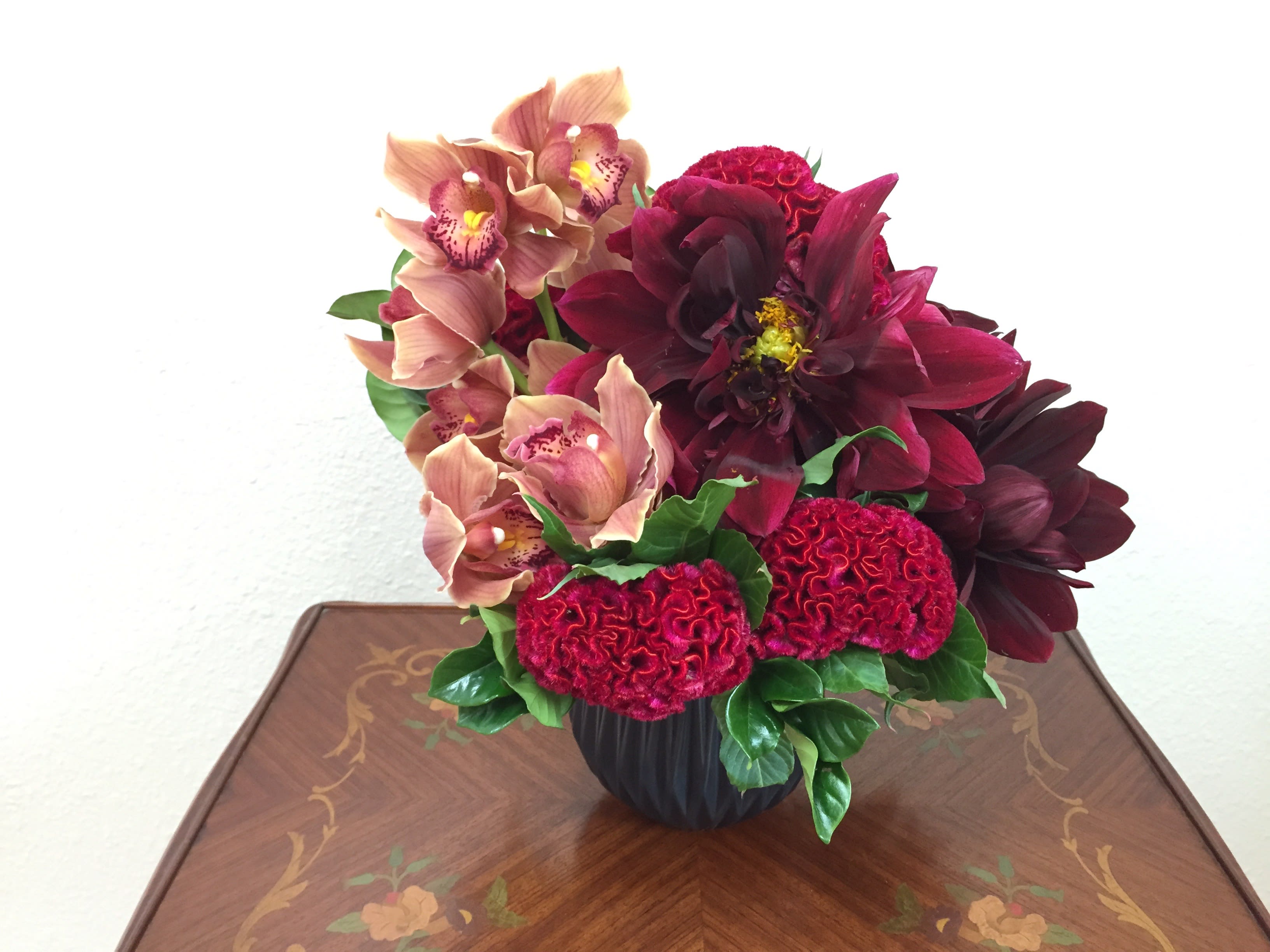 Deep red and peach floral arrangement in a black vase