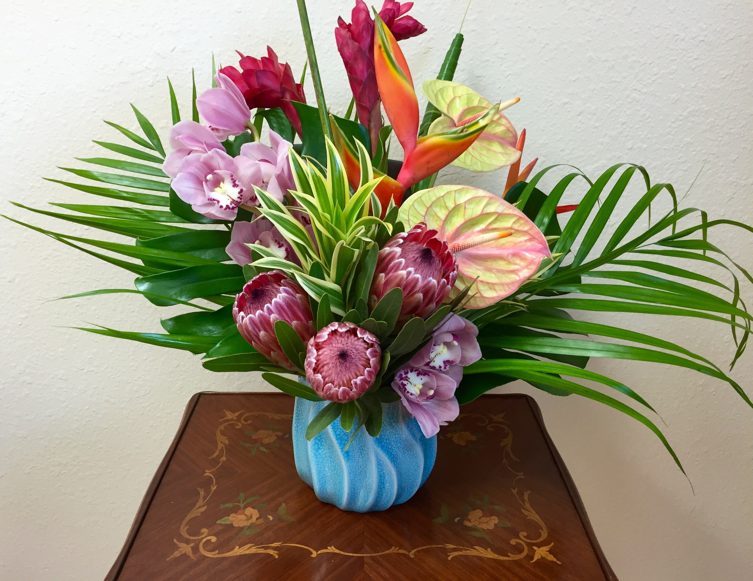Tropical bouquet with orchids, protea, and anthuriums in a blue vase