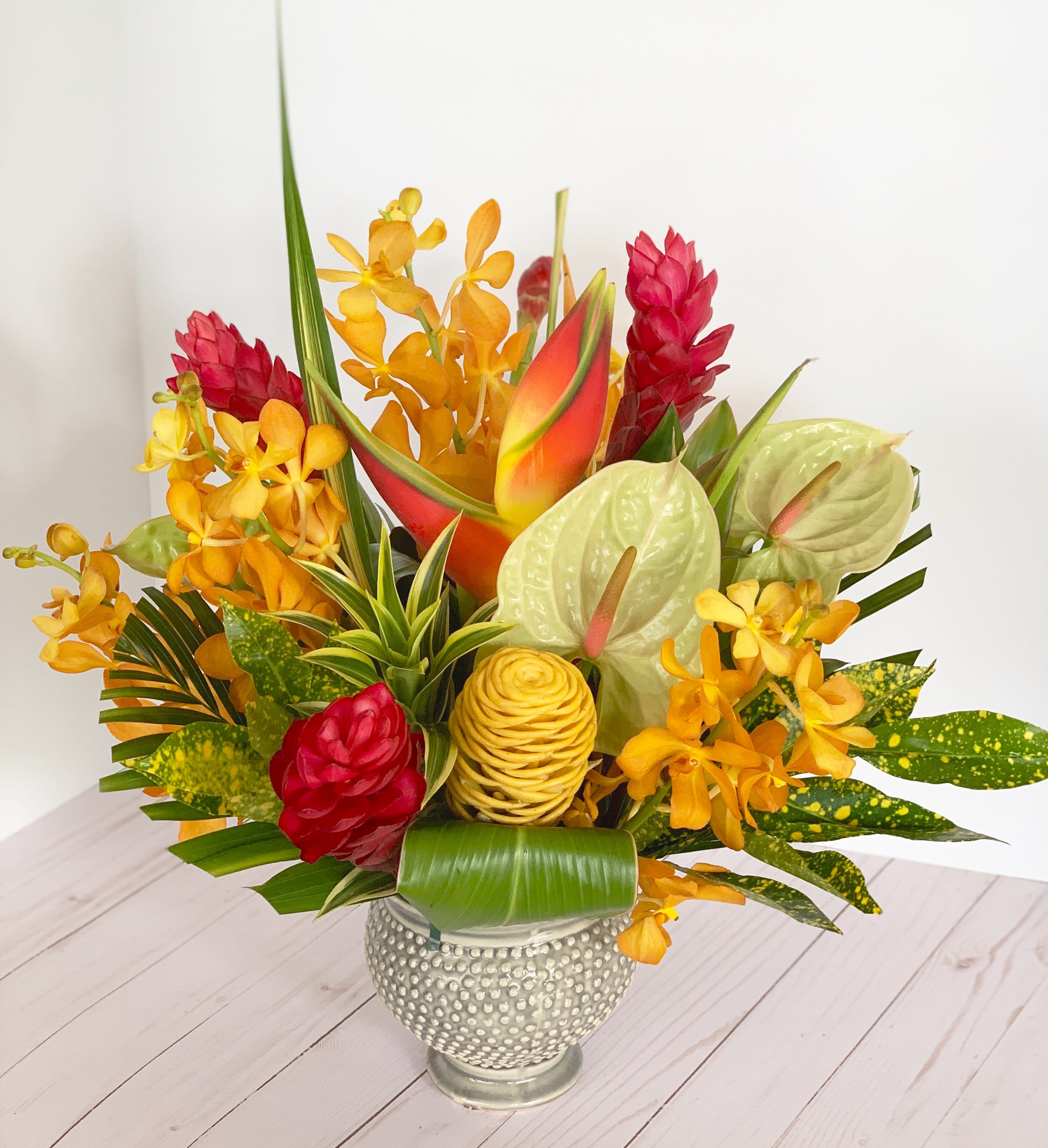 Tropical flower arrangement in a textured silver vase with red, orange, and green blooms