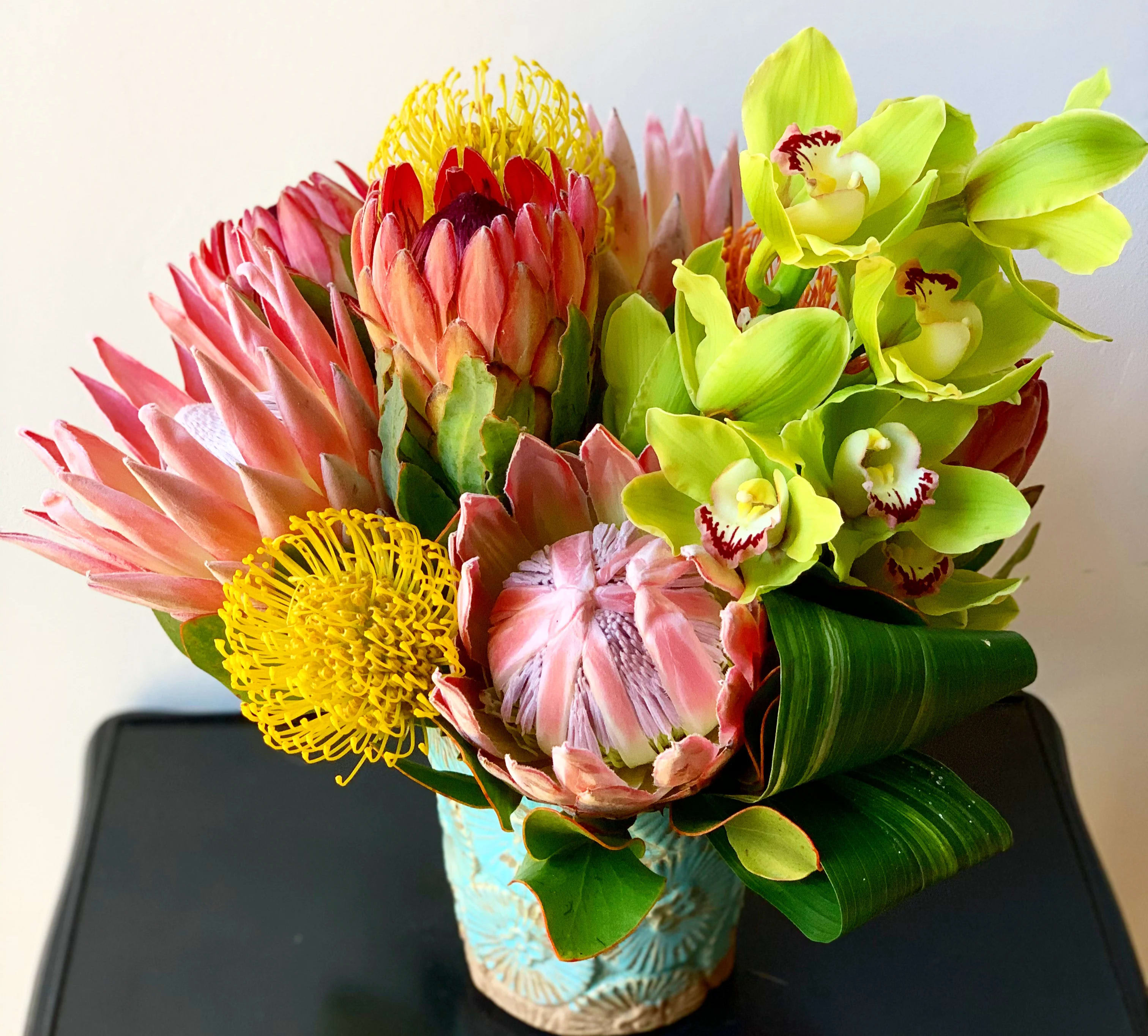 Bouquet of pink protea and green orchids in a blue vase