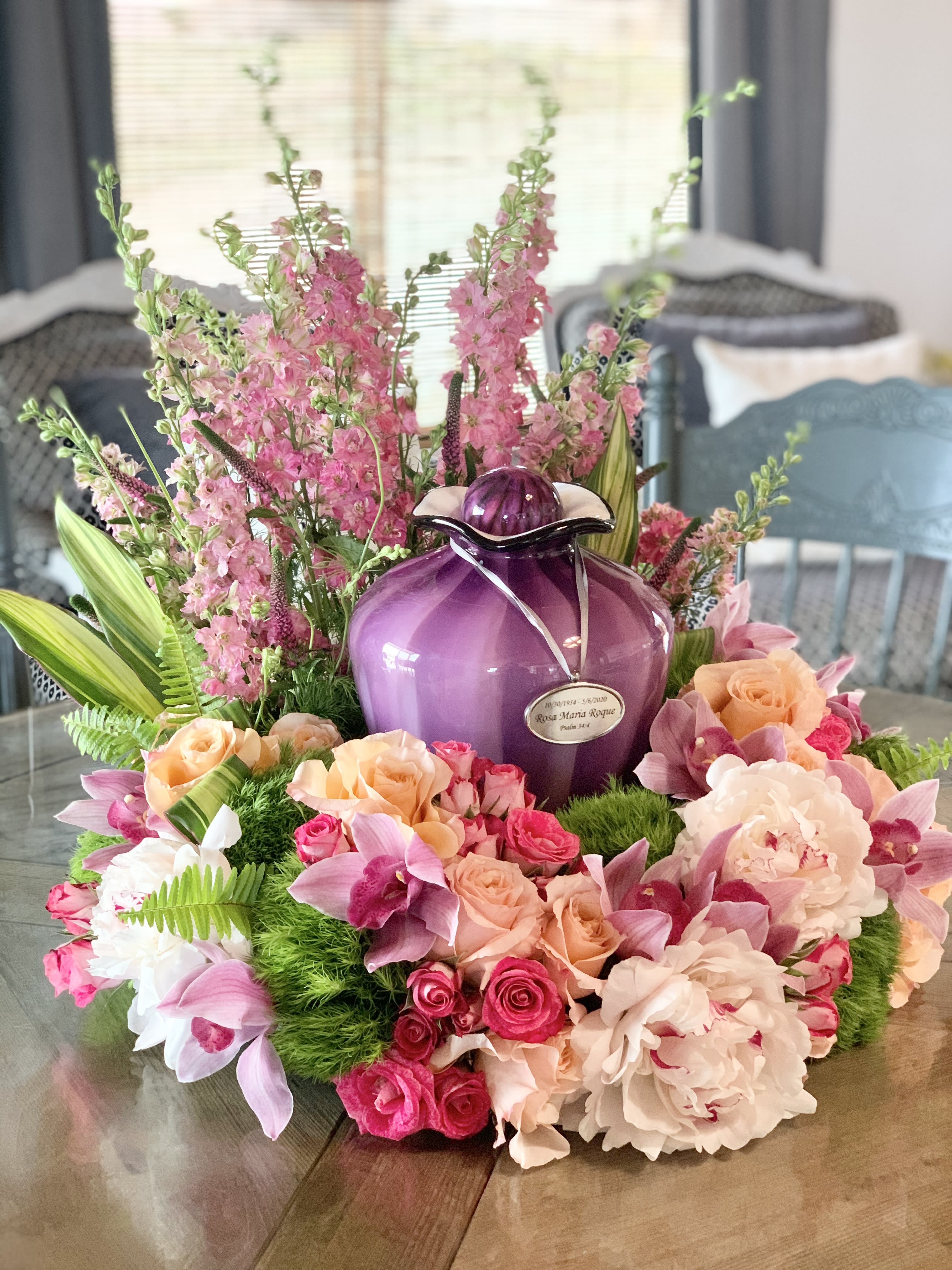 Pink and peach floral arrangement around a purple urn on a table