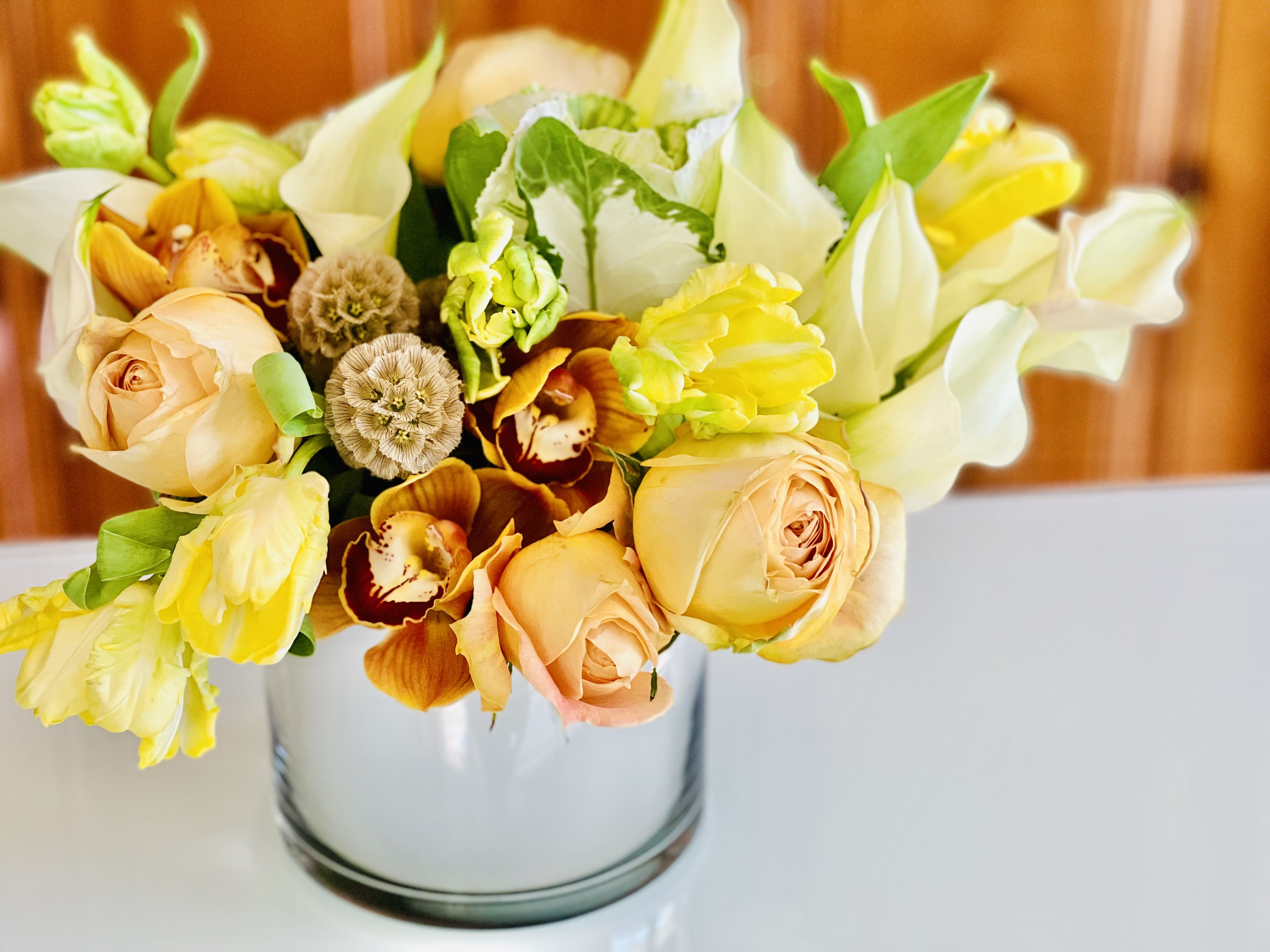 Bouquet of peach roses, yellow blooms, and white flowers in a glass vase