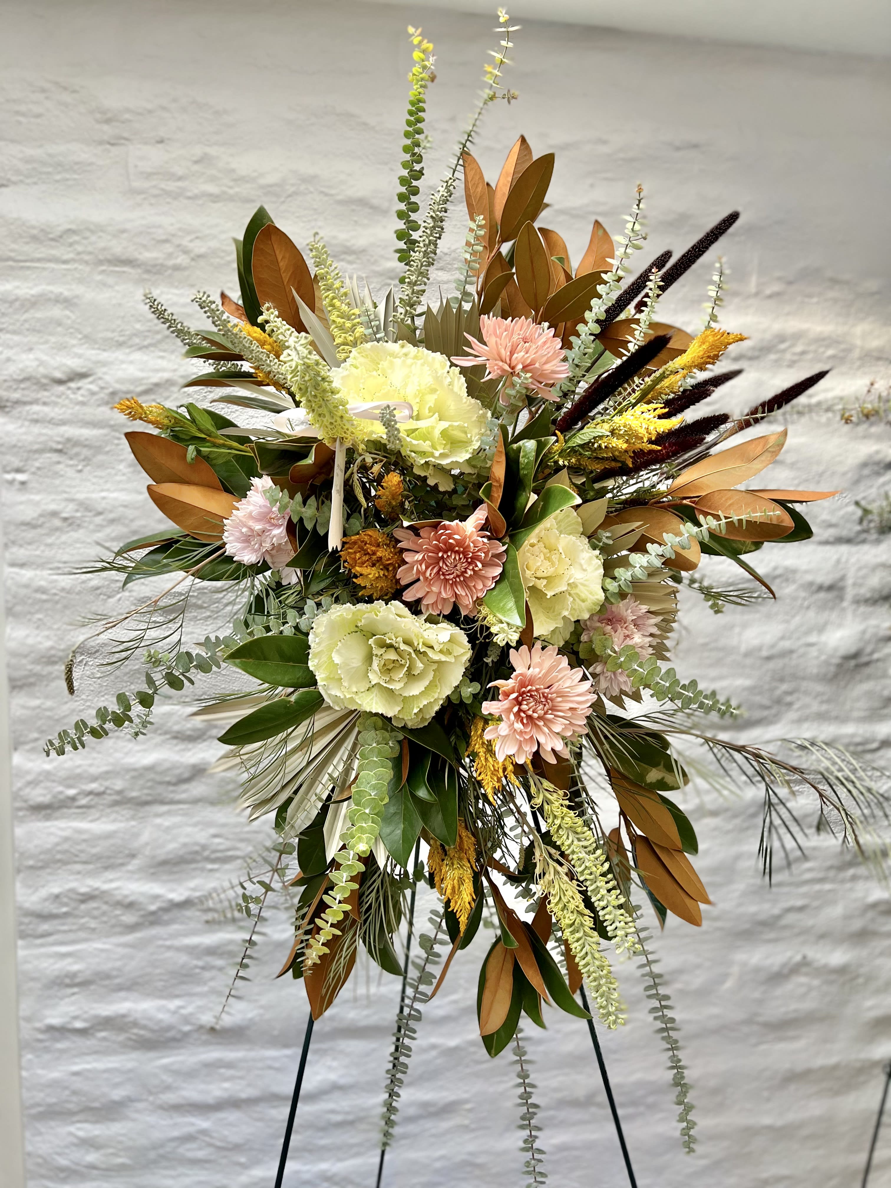 Tall floral spray with pale blooms and copper-toned foliage on a stand