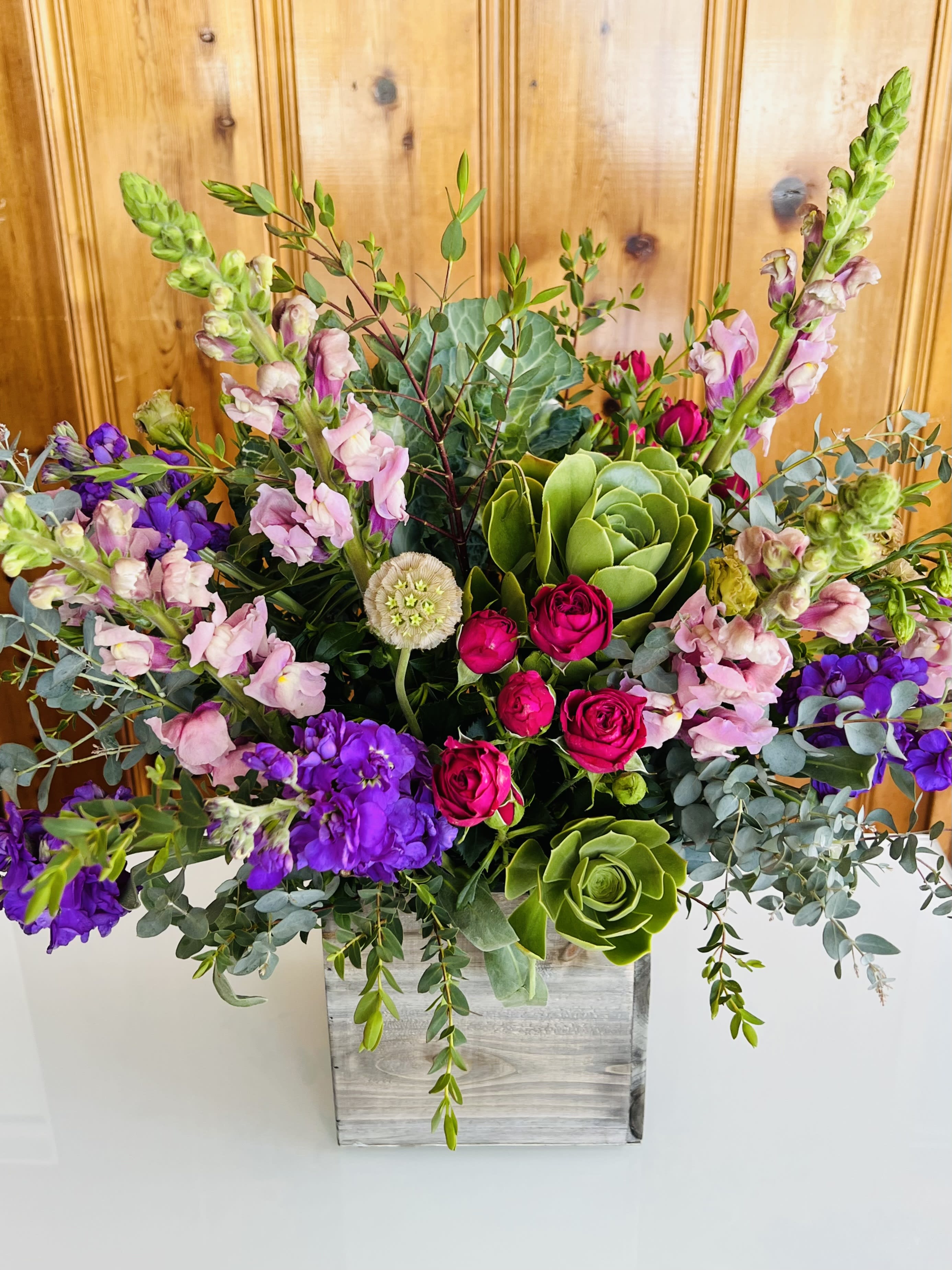 Mixed bouquet with pink roses, purple blooms, and green succulents in a wooden box