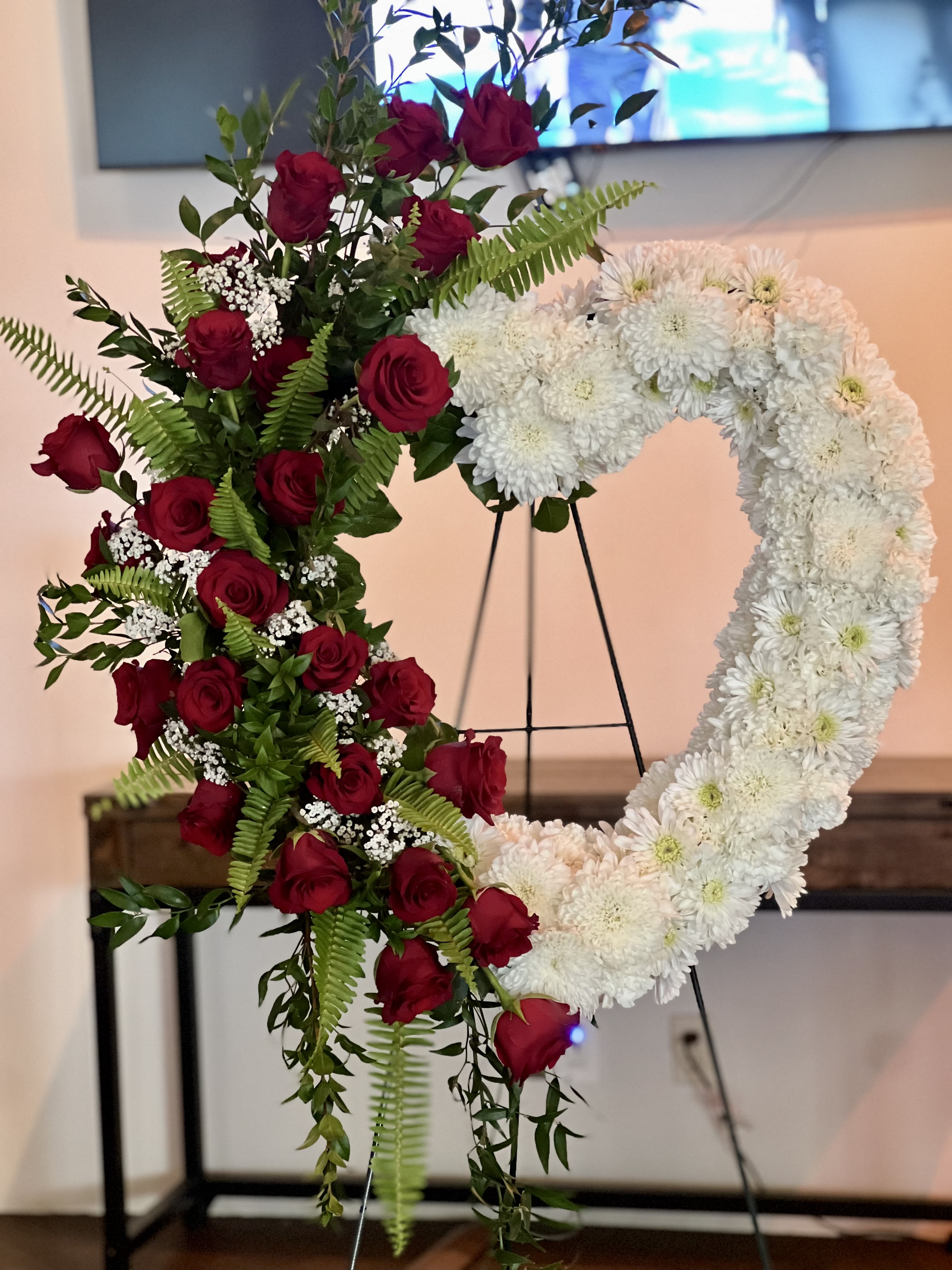 Heart-shaped floral wreath with red roses and white chrysanthemums on an easel