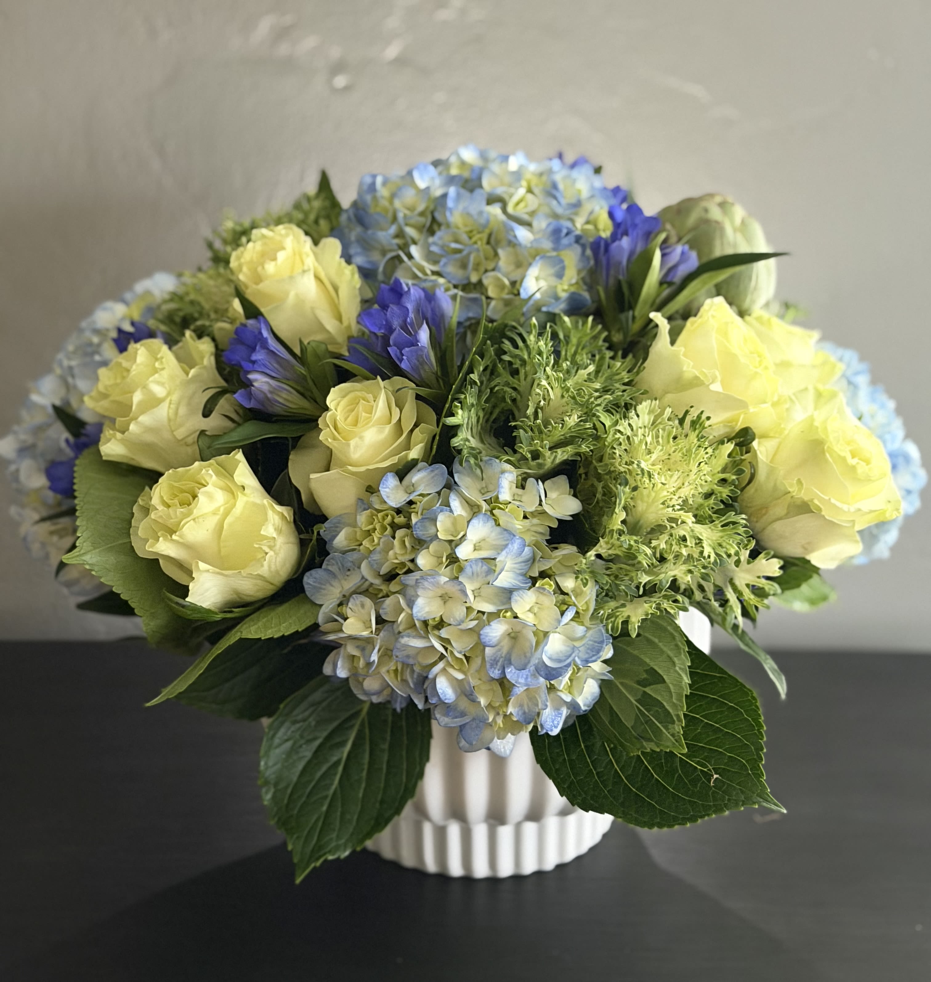 Yellow roses and blue hydrangeas in a white vase