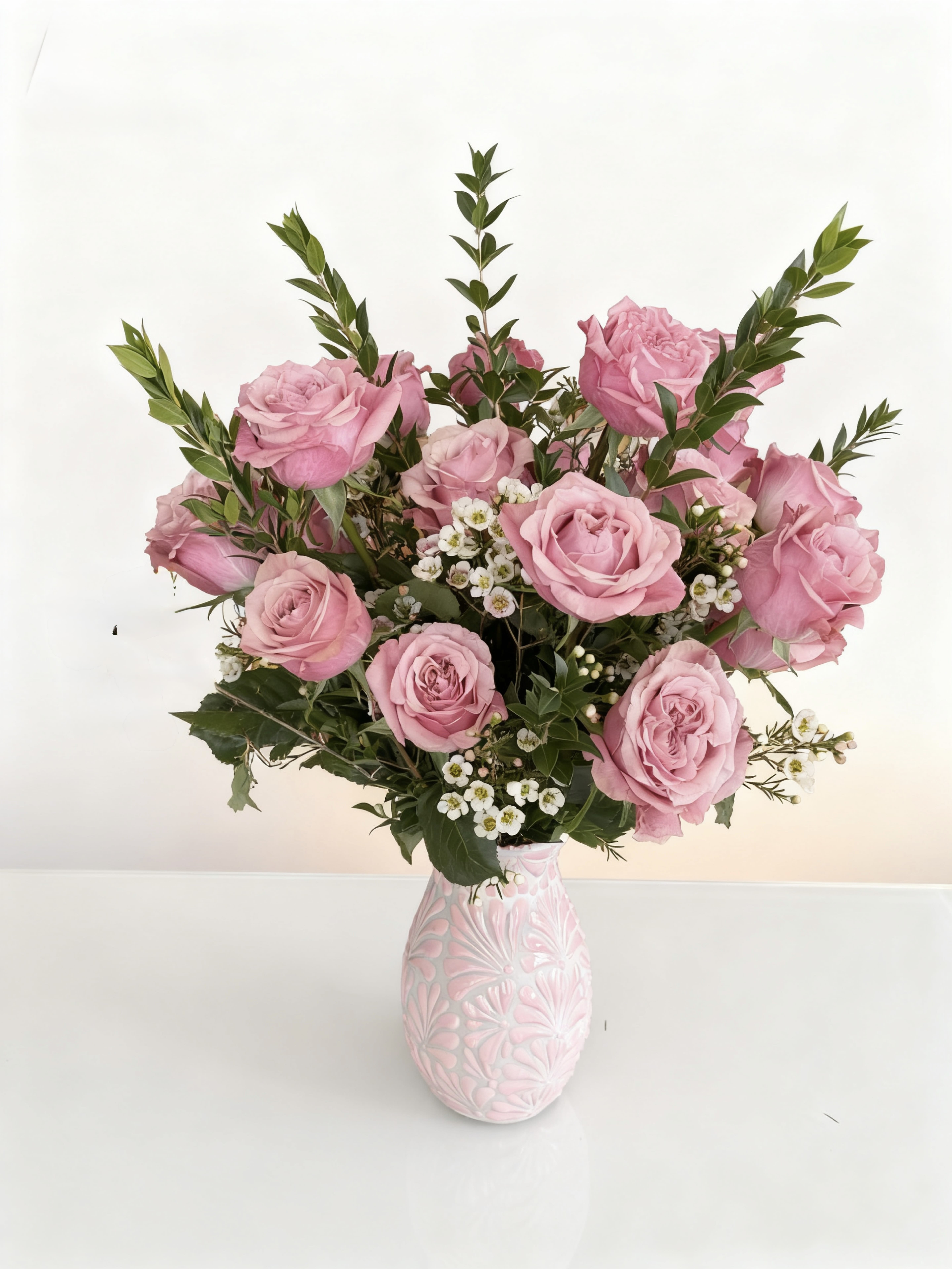 Pink roses arranged in a patterned vase with small white filler flowers