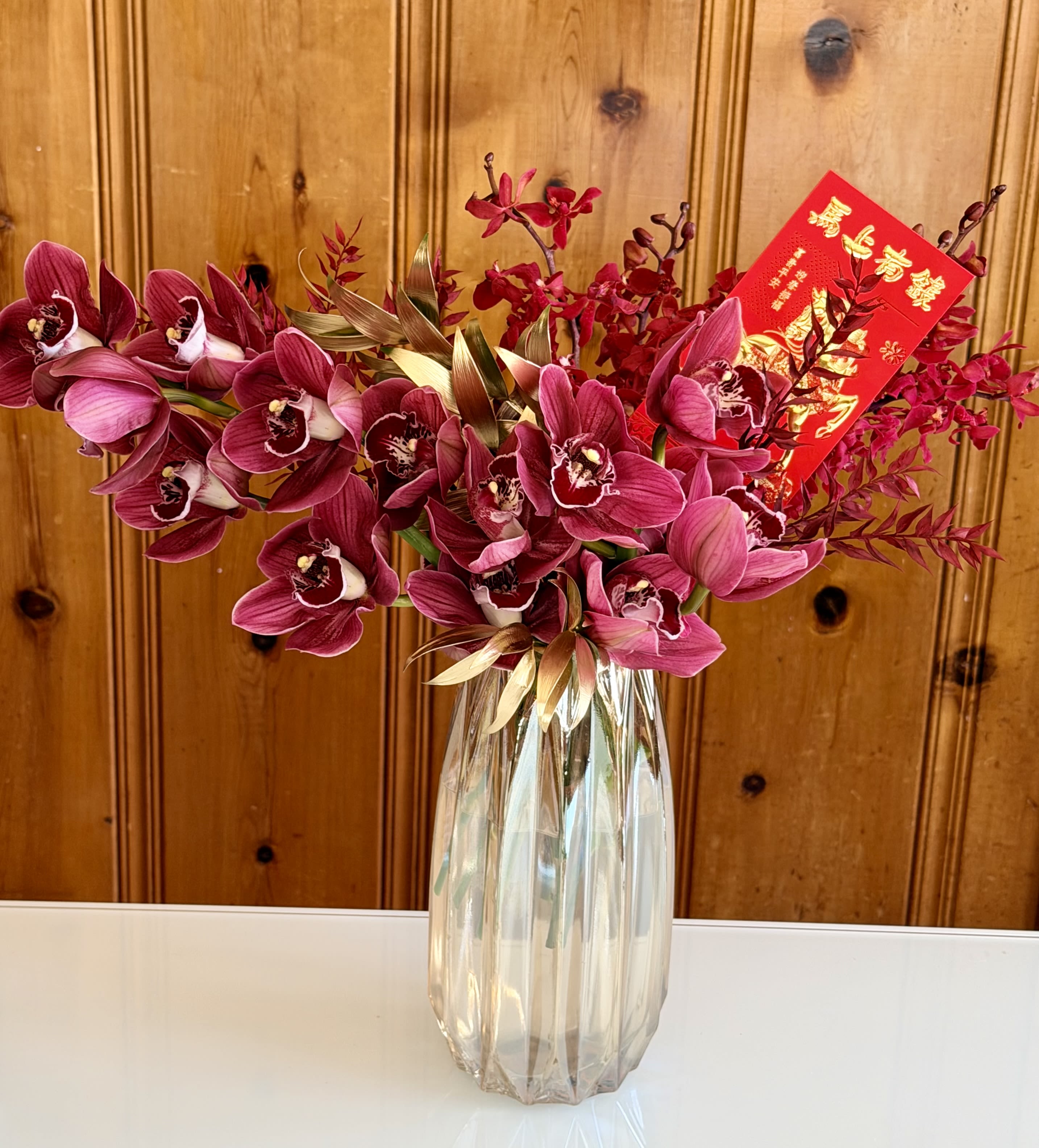 Pink orchids arranged in a clear glass vase with a red envelope card