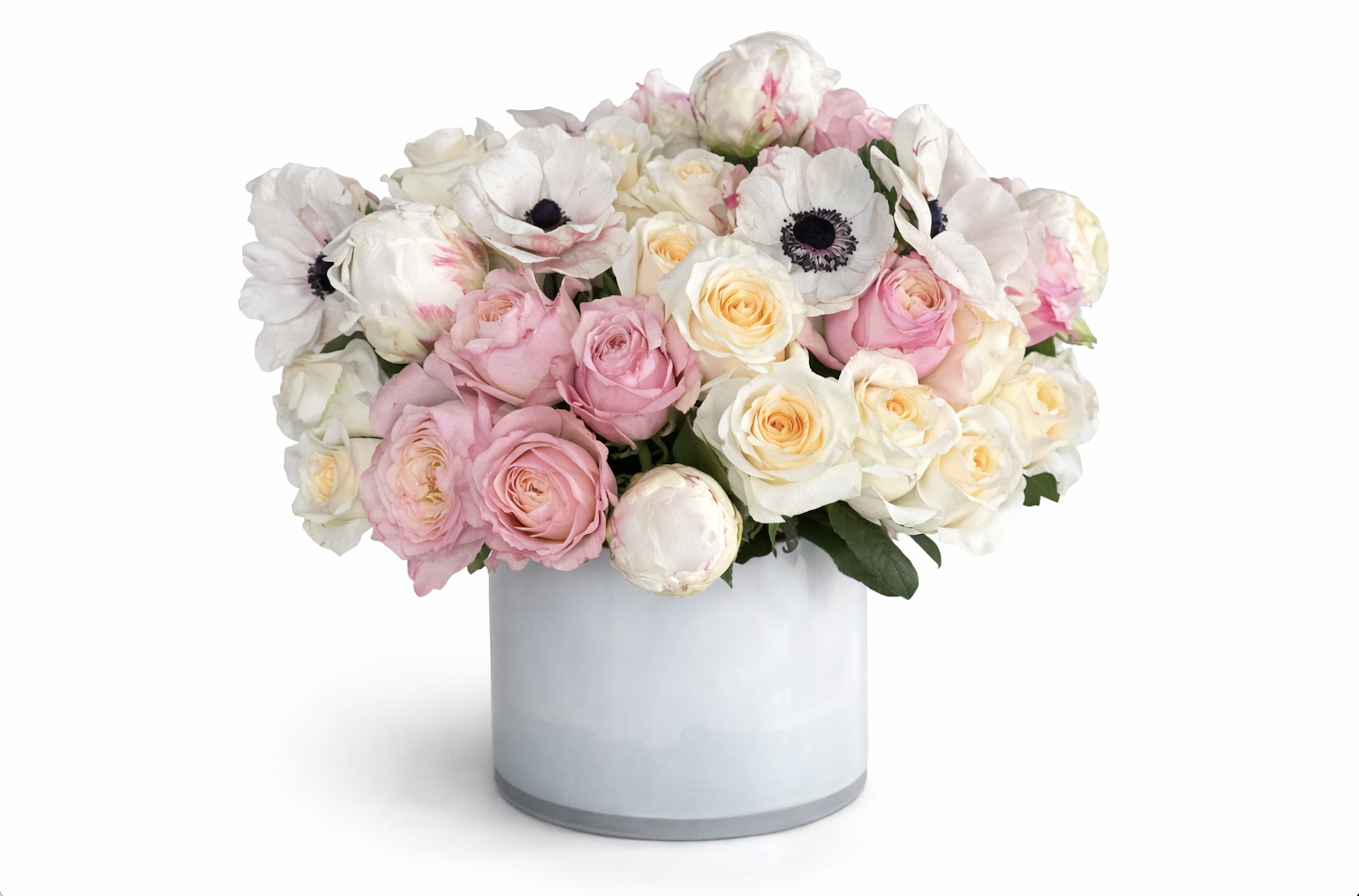 Low pastel arrangement of pink and cream roses with white anemones in a white cylinder vase