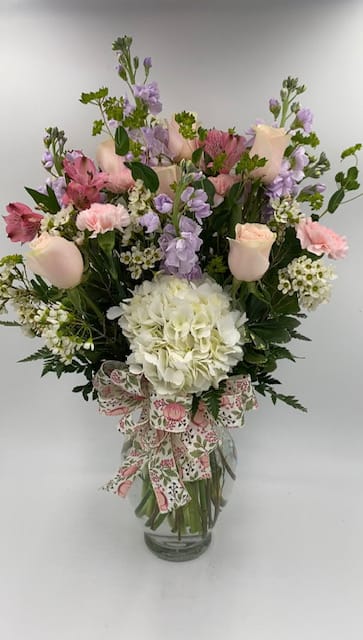 Mixed pink and lavender bouquet in a glass vase with a floral ribbon