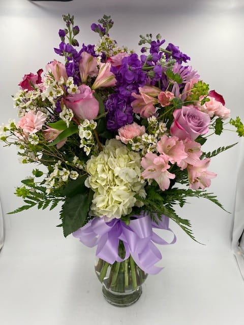 Mixed pink and purple bouquet in a clear glass vase with a lavender ribbon
