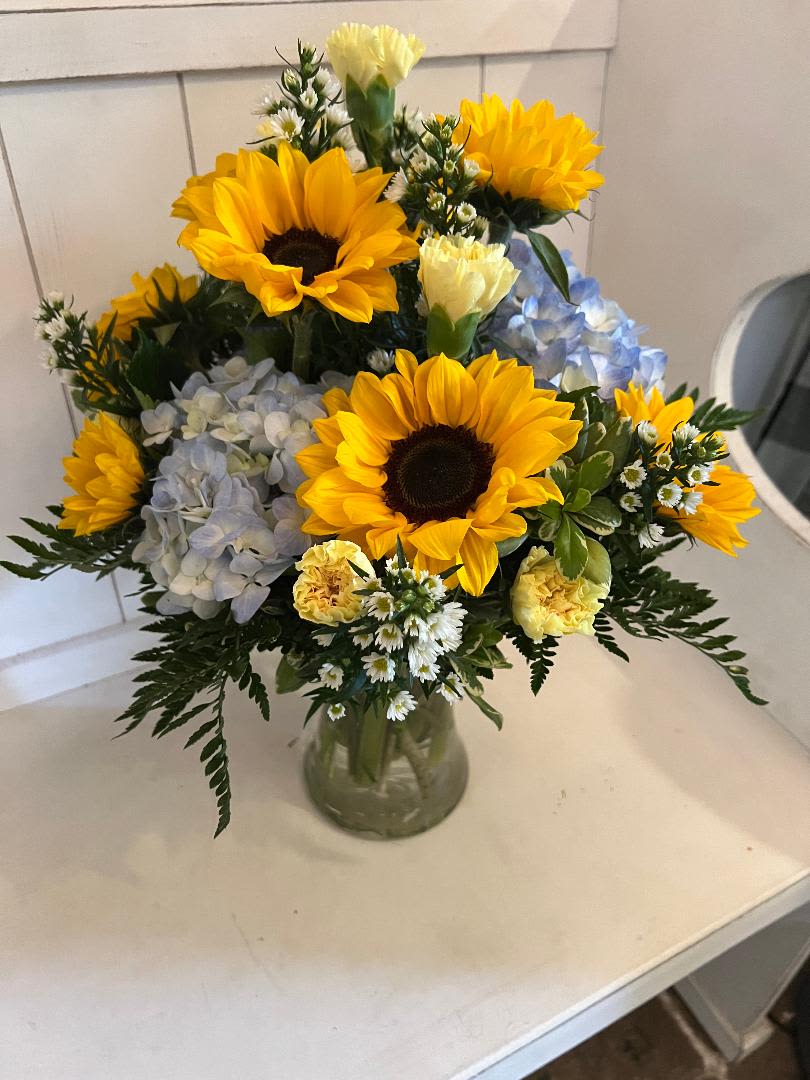 Bouquet of sunflowers, hydrangeas, and small white flowers in a glass vase