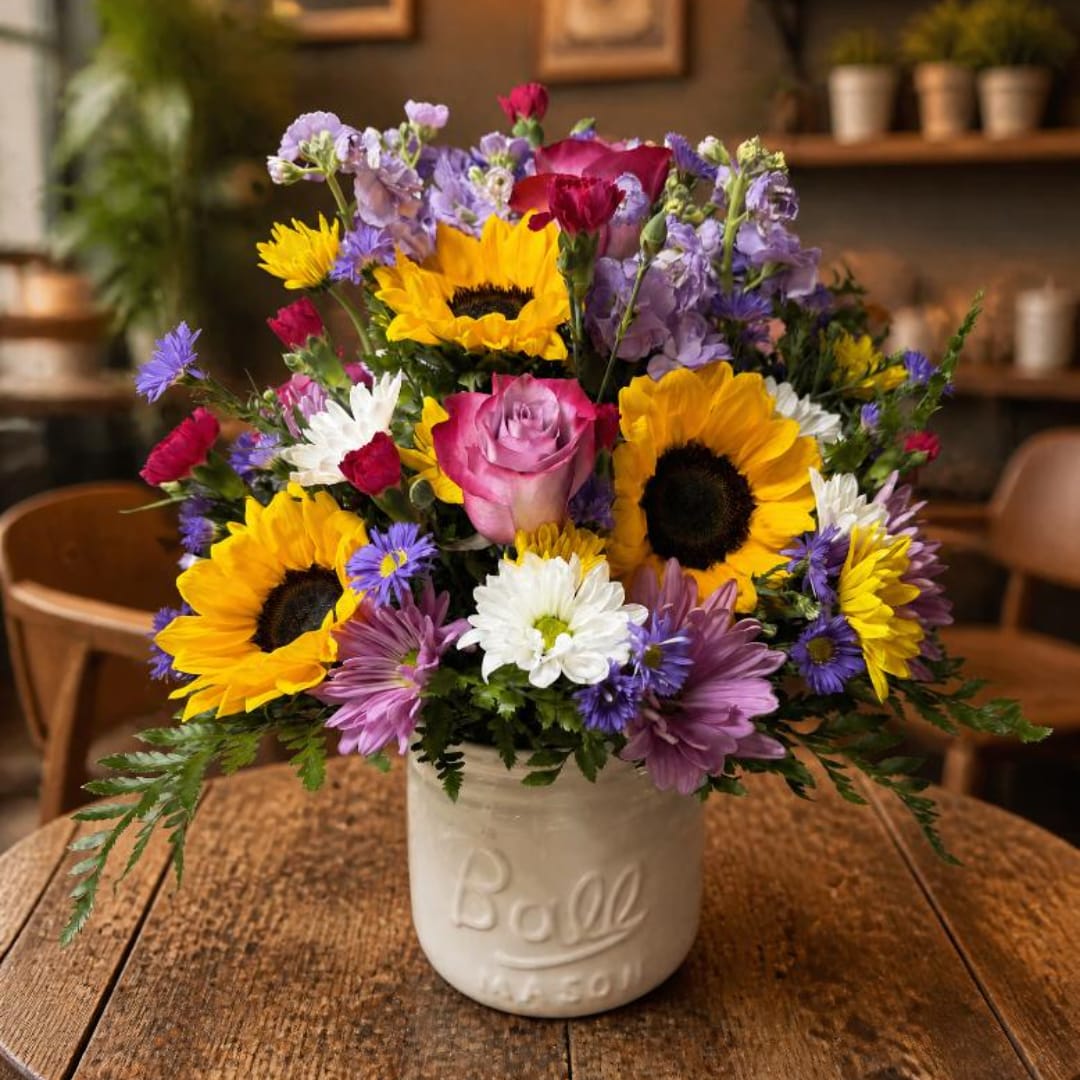 Mixed bouquet with sunflowers, roses, and daisies in a white ceramic jar