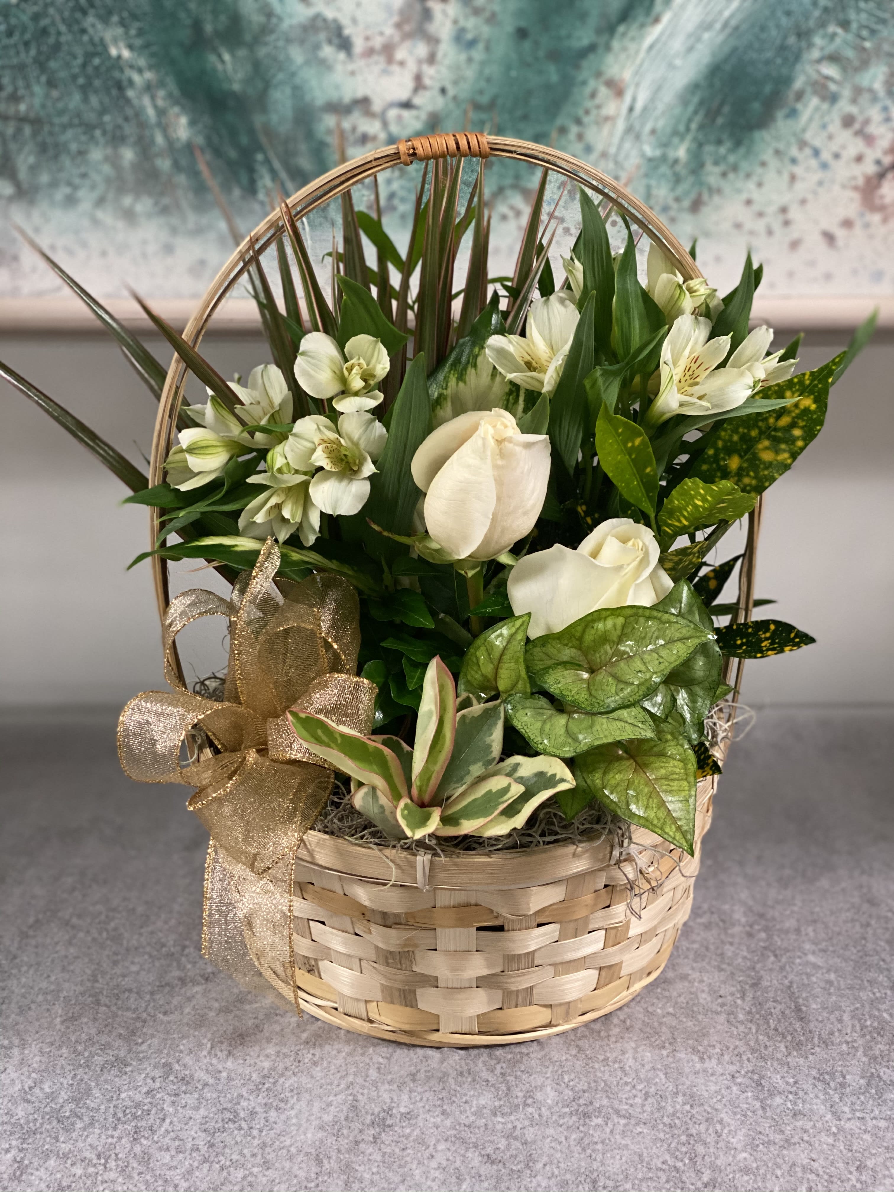 Basket arrangement with white flowers and green foliage, tied with a gold ribbon